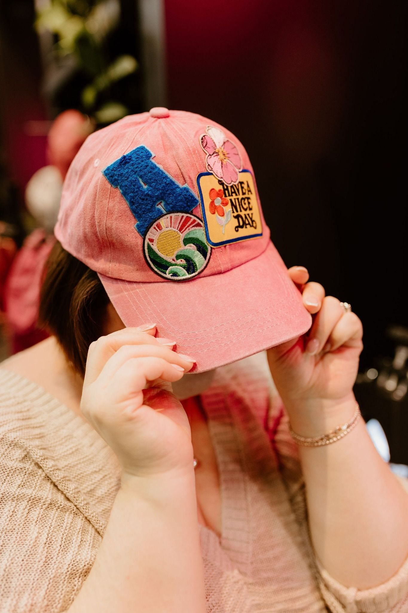 Person in a pink cap with colorful patches, holding the brim down against their face.