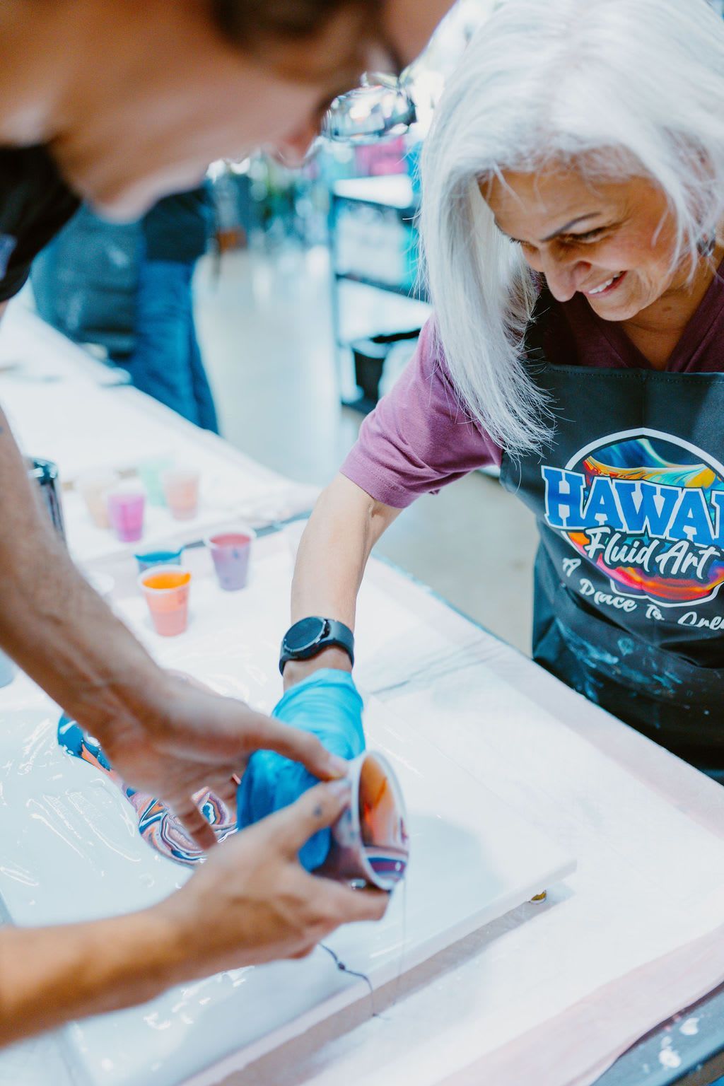 Woman in a white wig and apron painting on a white table at a craft event