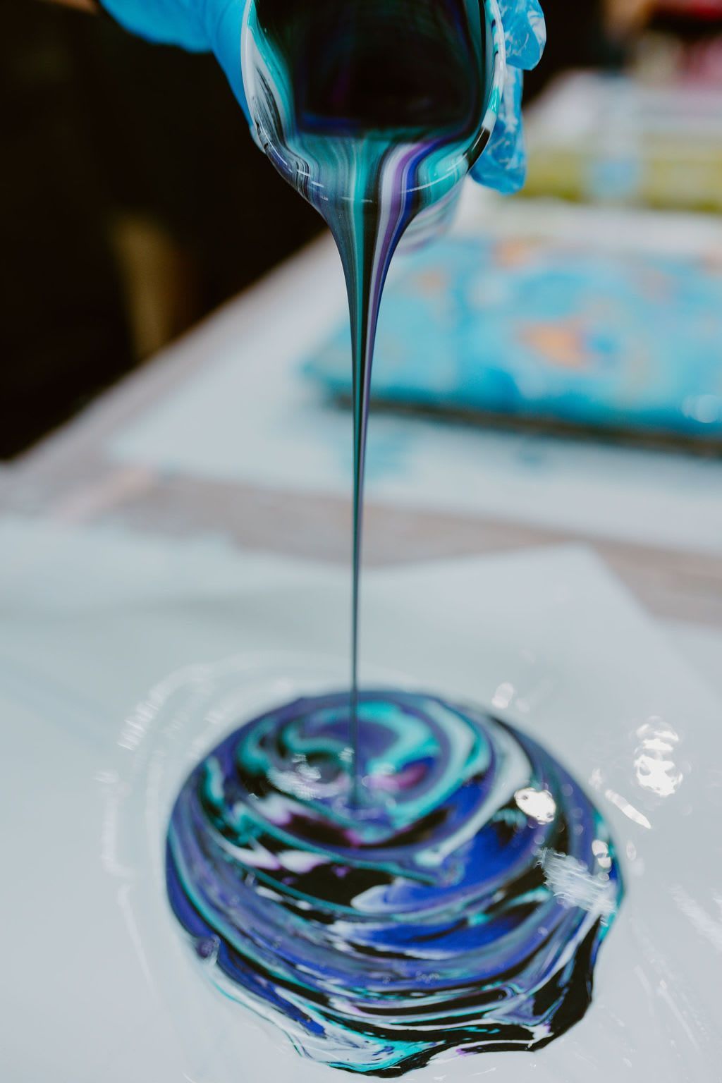 Colorful paint pouring onto a canvas, creating a swirling blue, purple, and black pattern