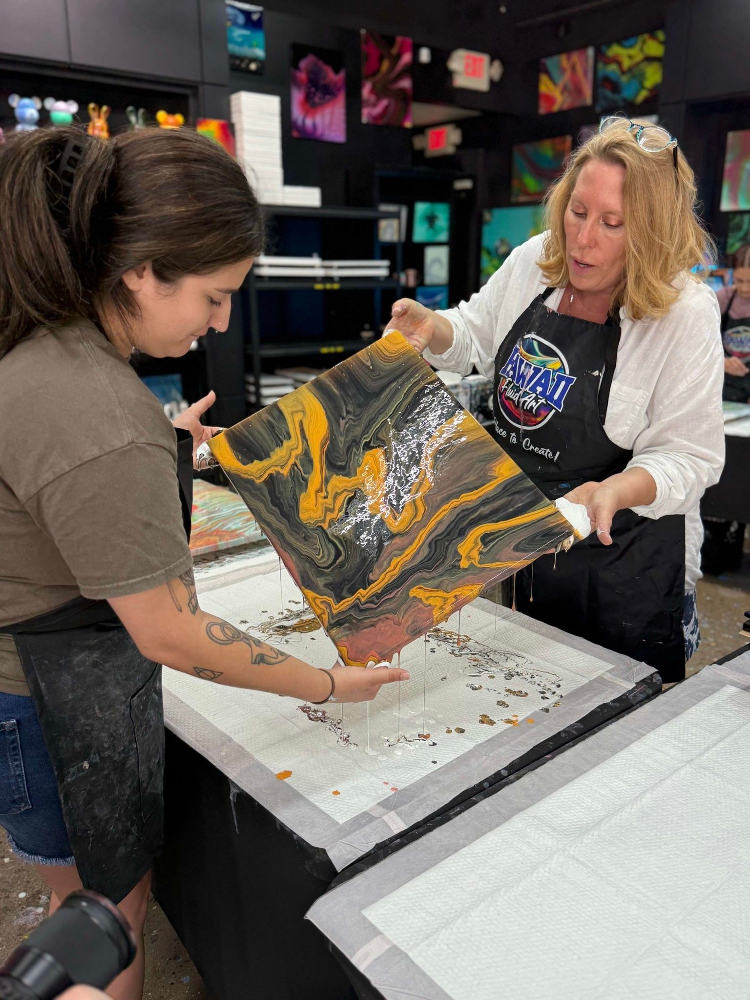 Two people carefully handling a colorful printed fabric in a workshop or classroom.