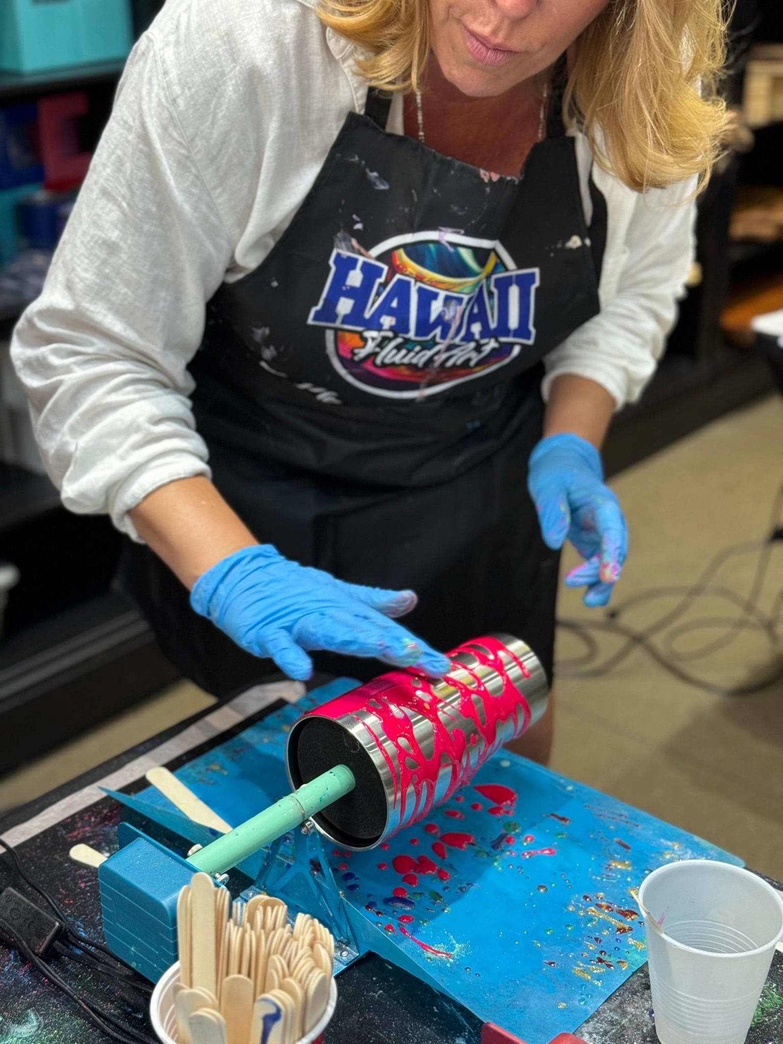 Person in gloves decorating a red roller-shaped craft on a table with paint and supplies.