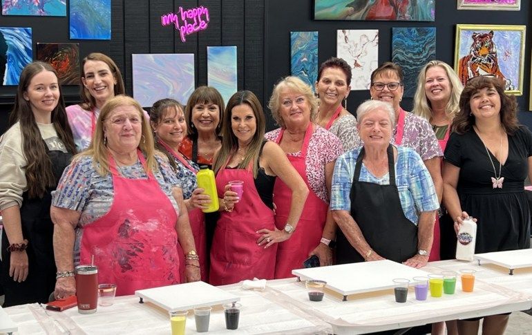Group of people posing in an art studio with colorful paintings and paint supplies on a table