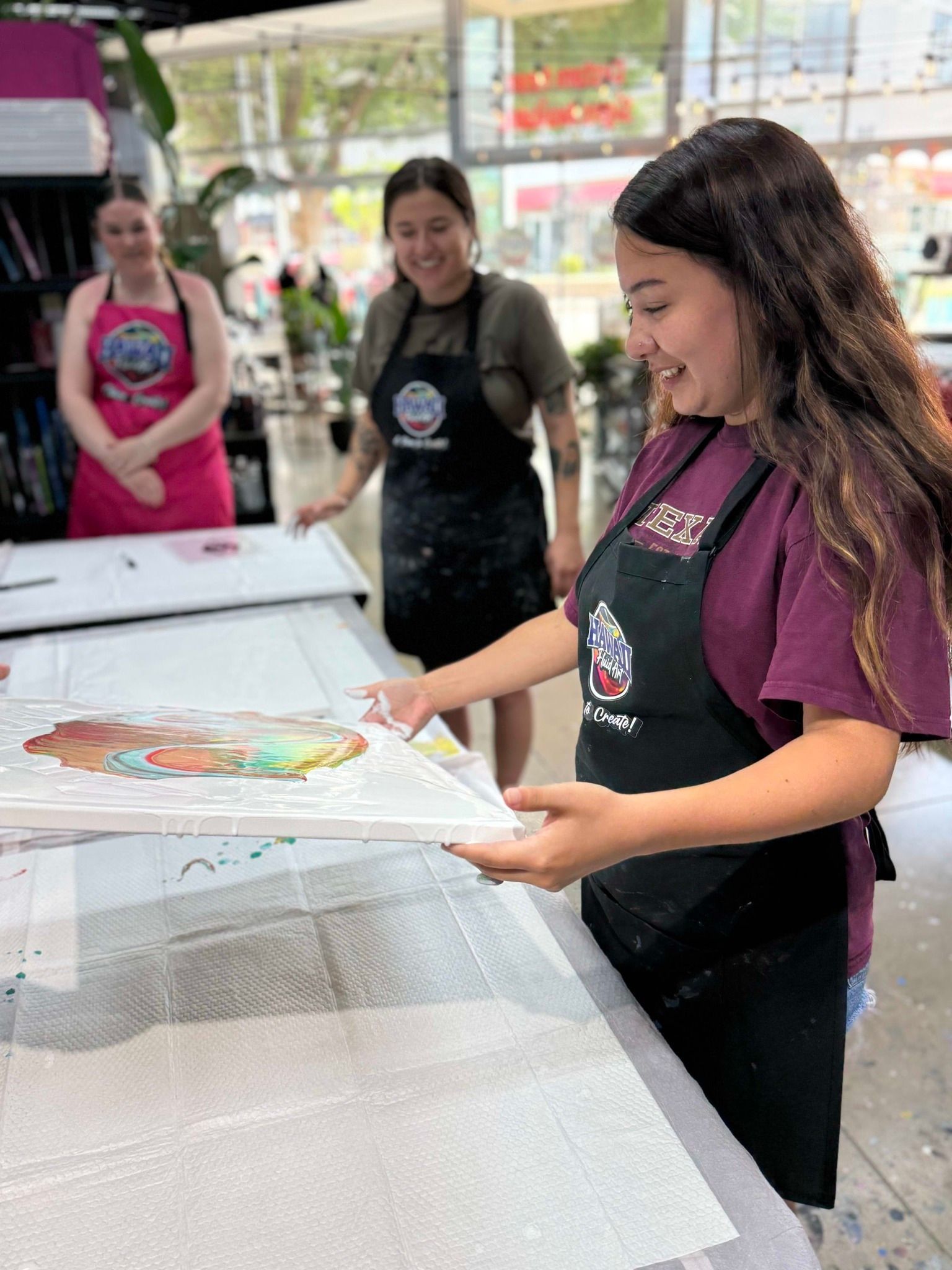 Woman in a maroon shirt and apron handling a large printed sheet at a workshop table.