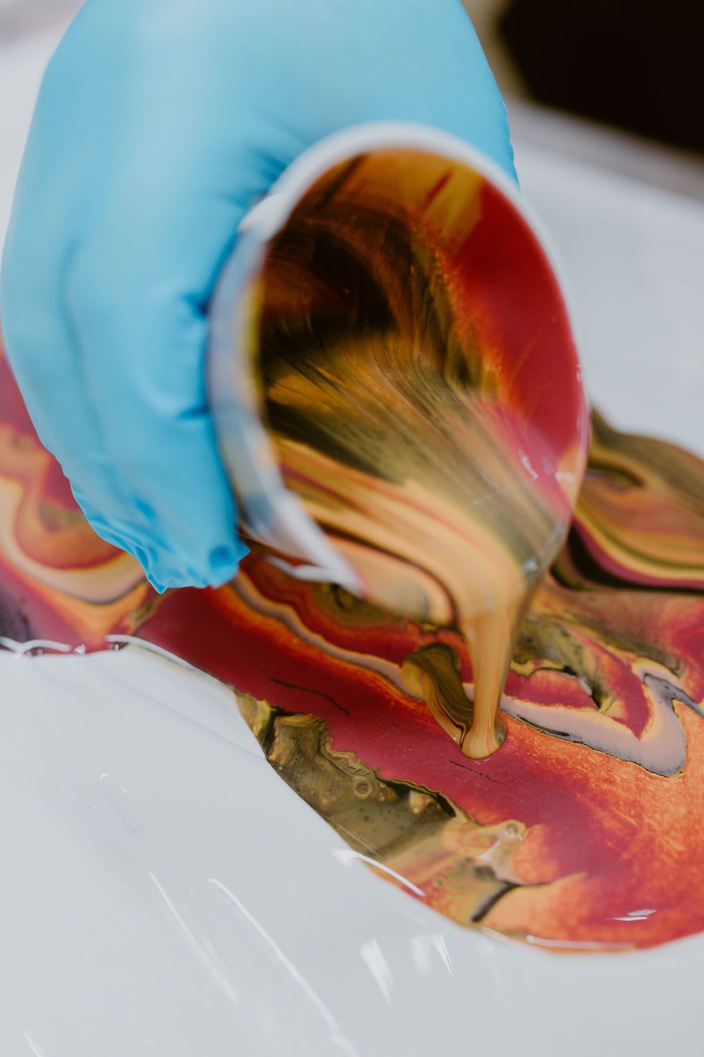 Gloved hand pouring colorful liquid paint onto a white surface, creating a marbled swirl
