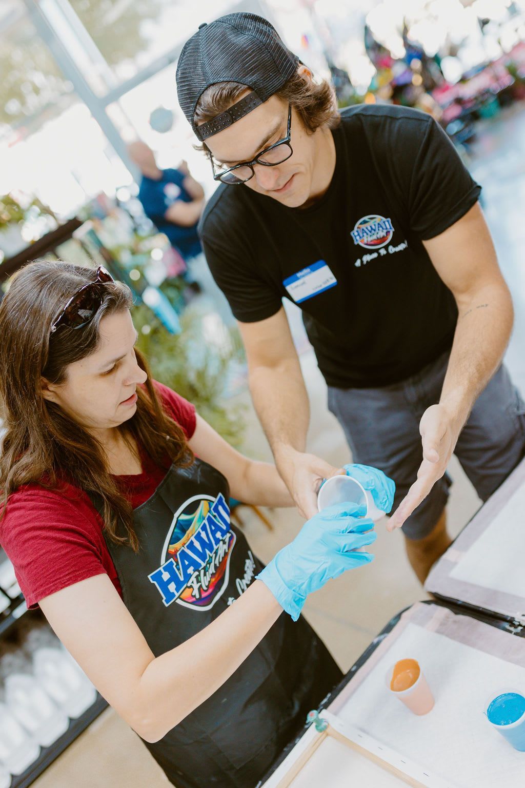 Two volunteers in gloves prepare items at a table during a community event.