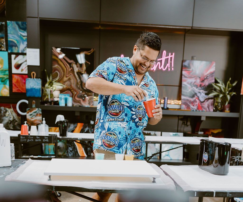 Man in blue floral shirt mixes ingredients at a kitchen counter in a bright studio set