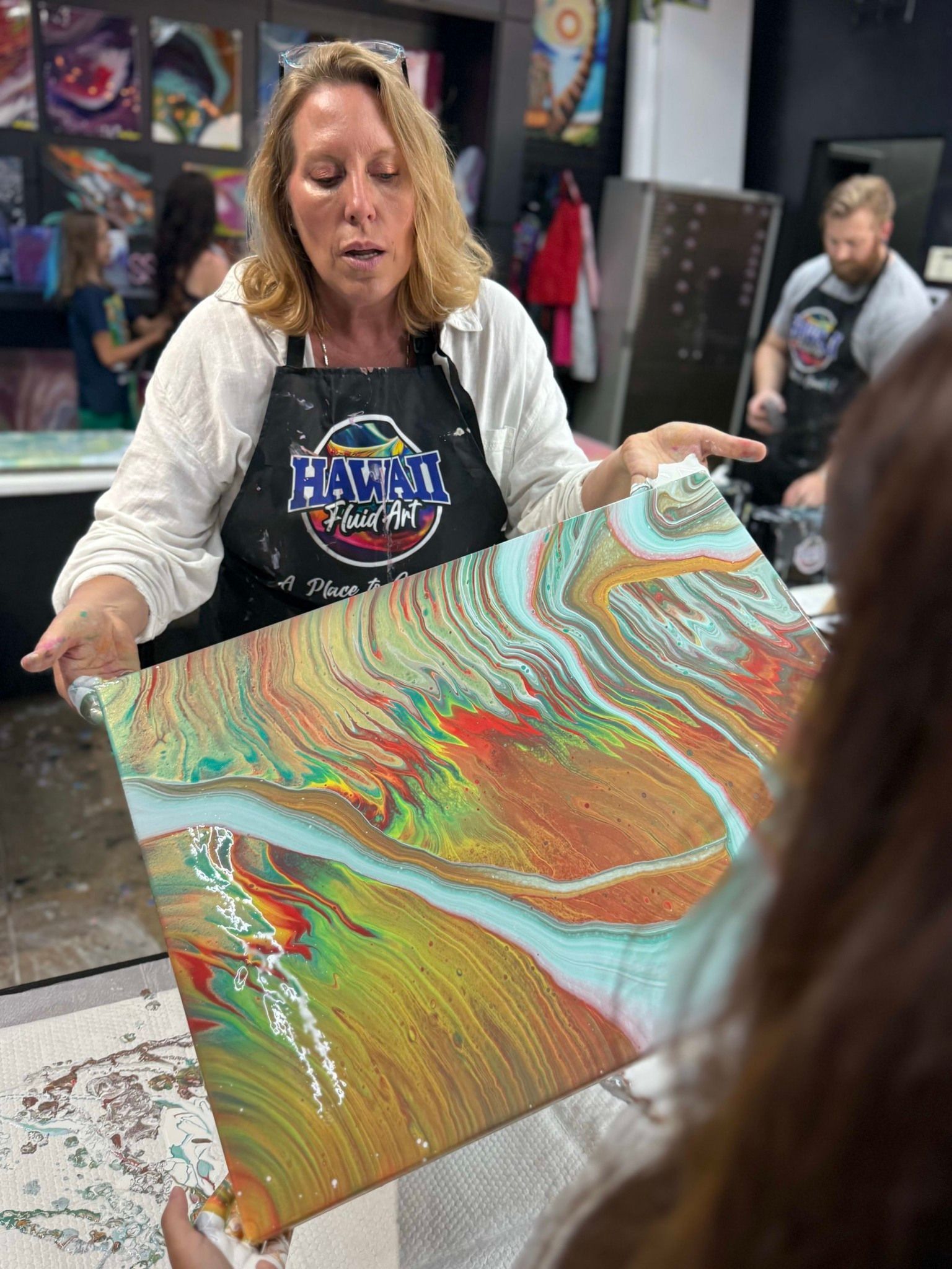 Woman in an art studio holding a colorful abstract painting with swirling red, green, and gold patterns