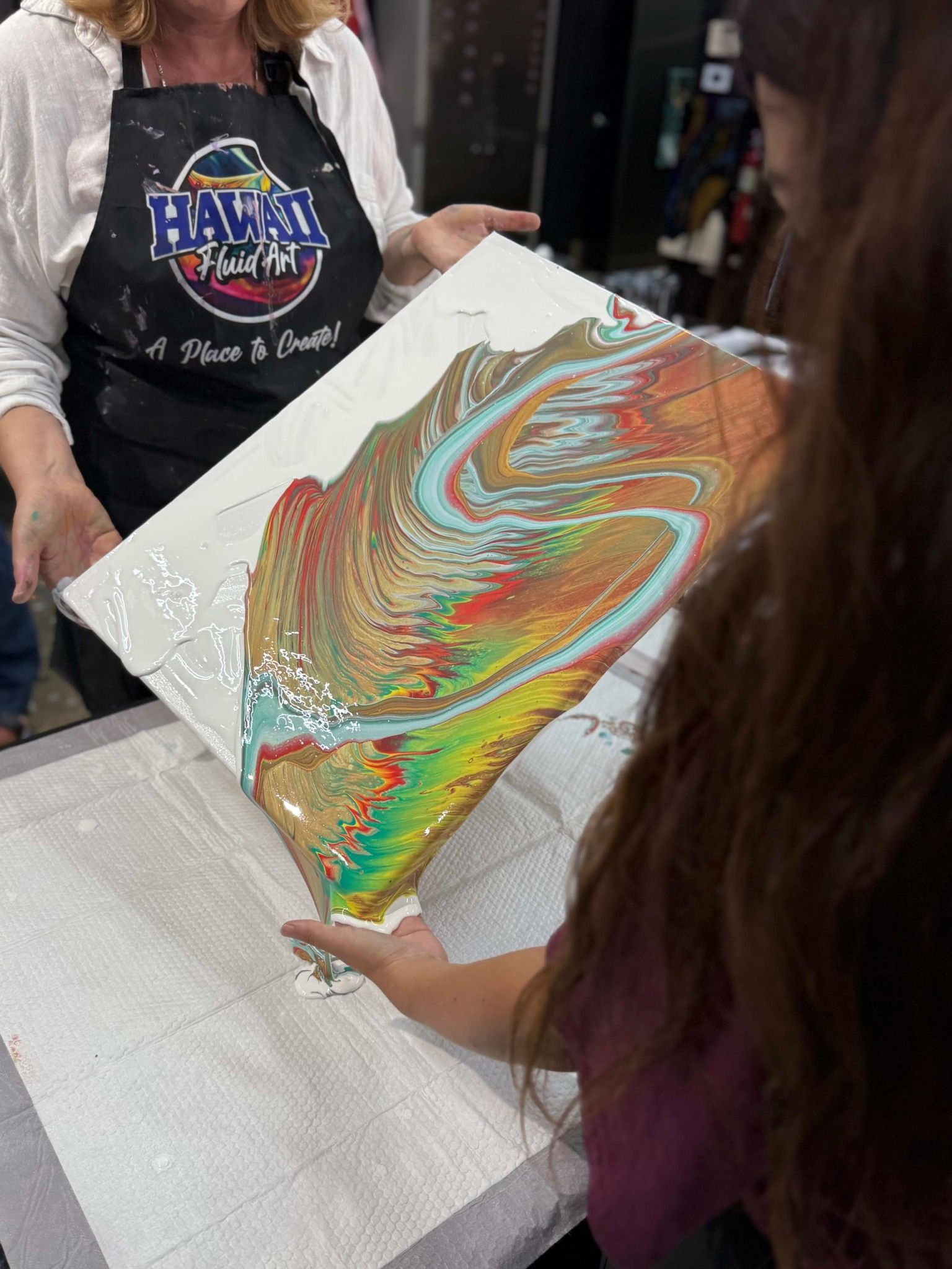 People unrolling a colorful abstract canvas print on a table in a shop.