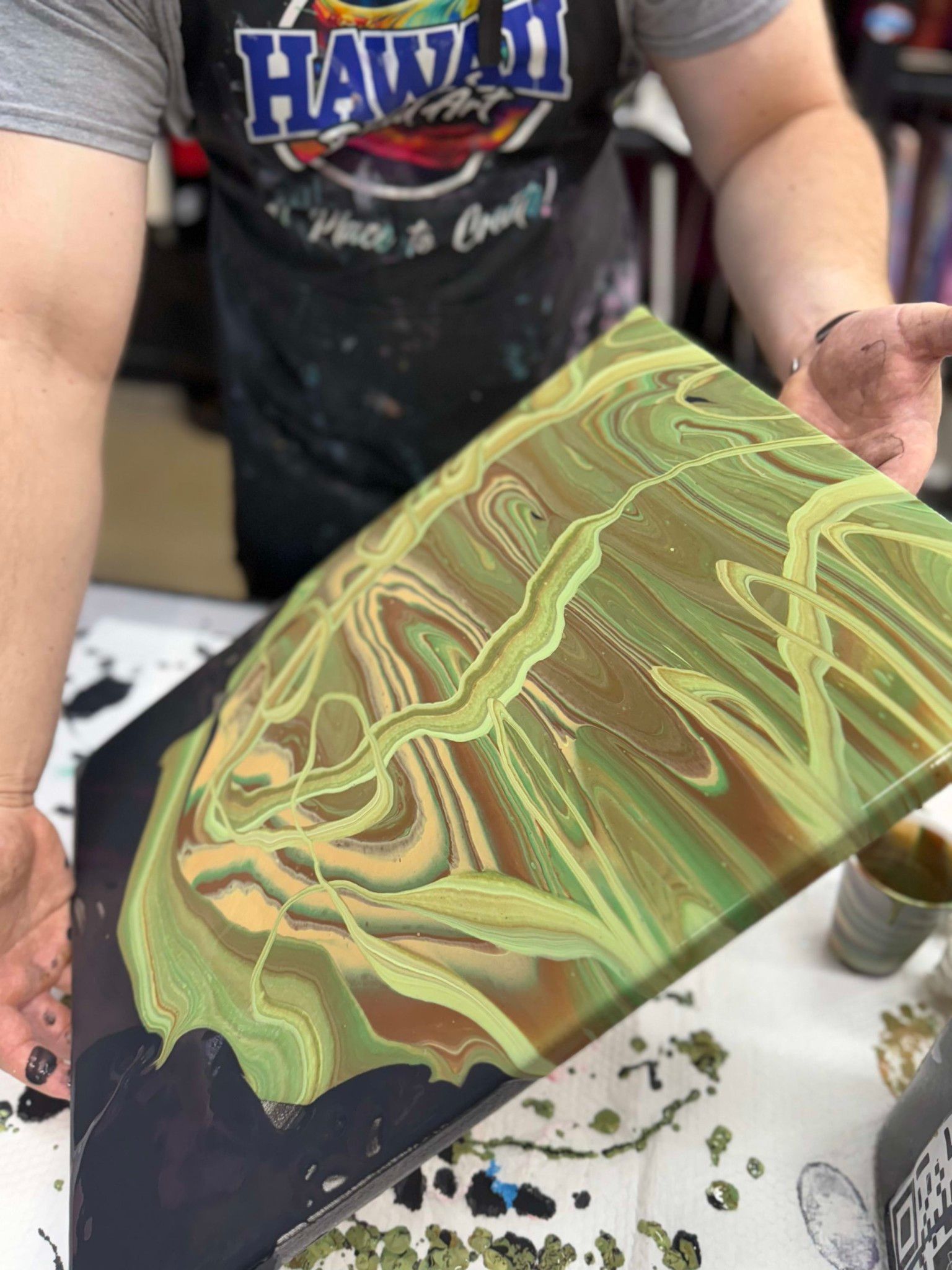 Person holding a green and black marbled resin art piece at a crafting table