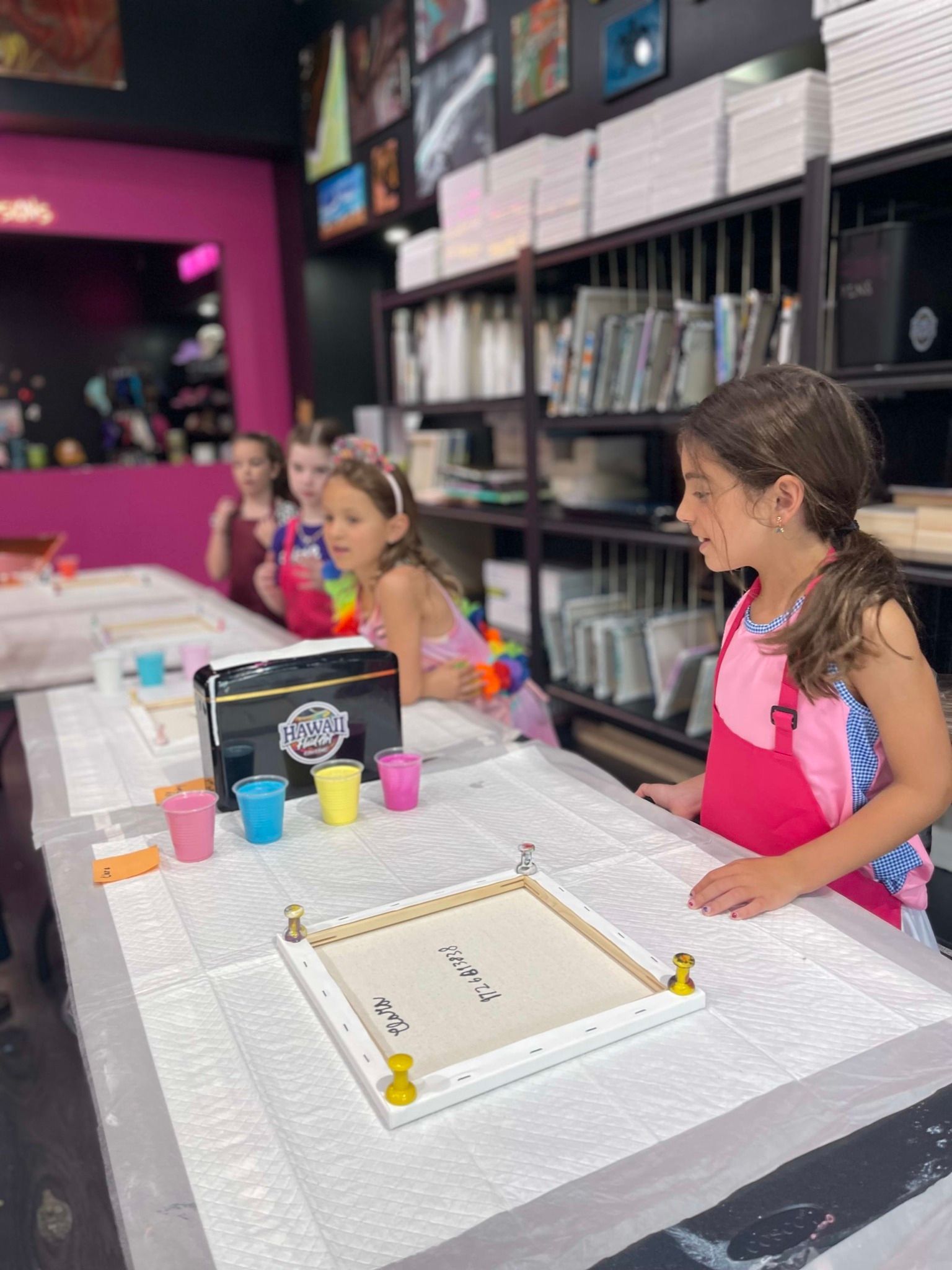 Children at a craft table with cups of paint in a colorful art studio