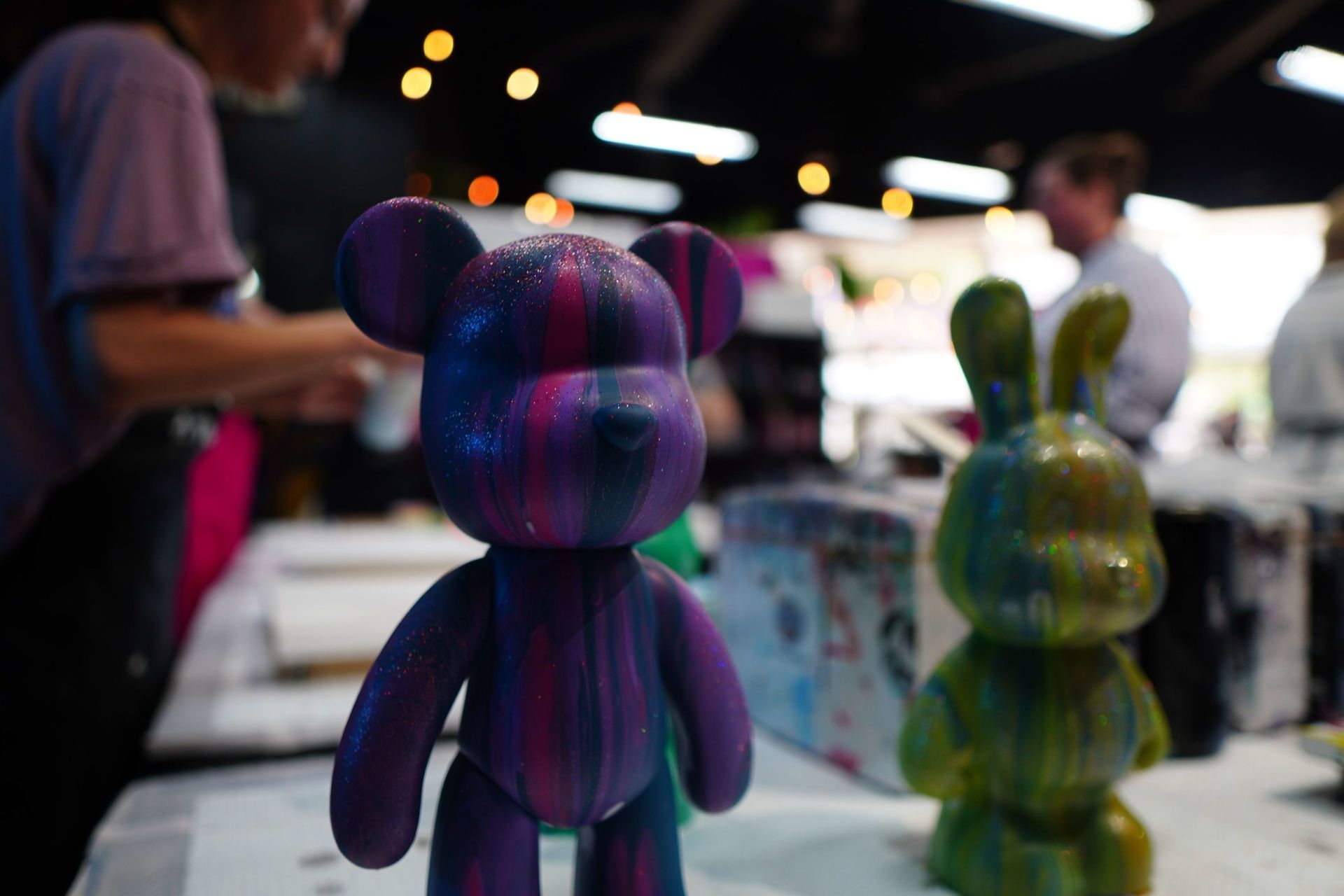 Colorful 3D-printed figurines on a table at an event, with people blurred in the background