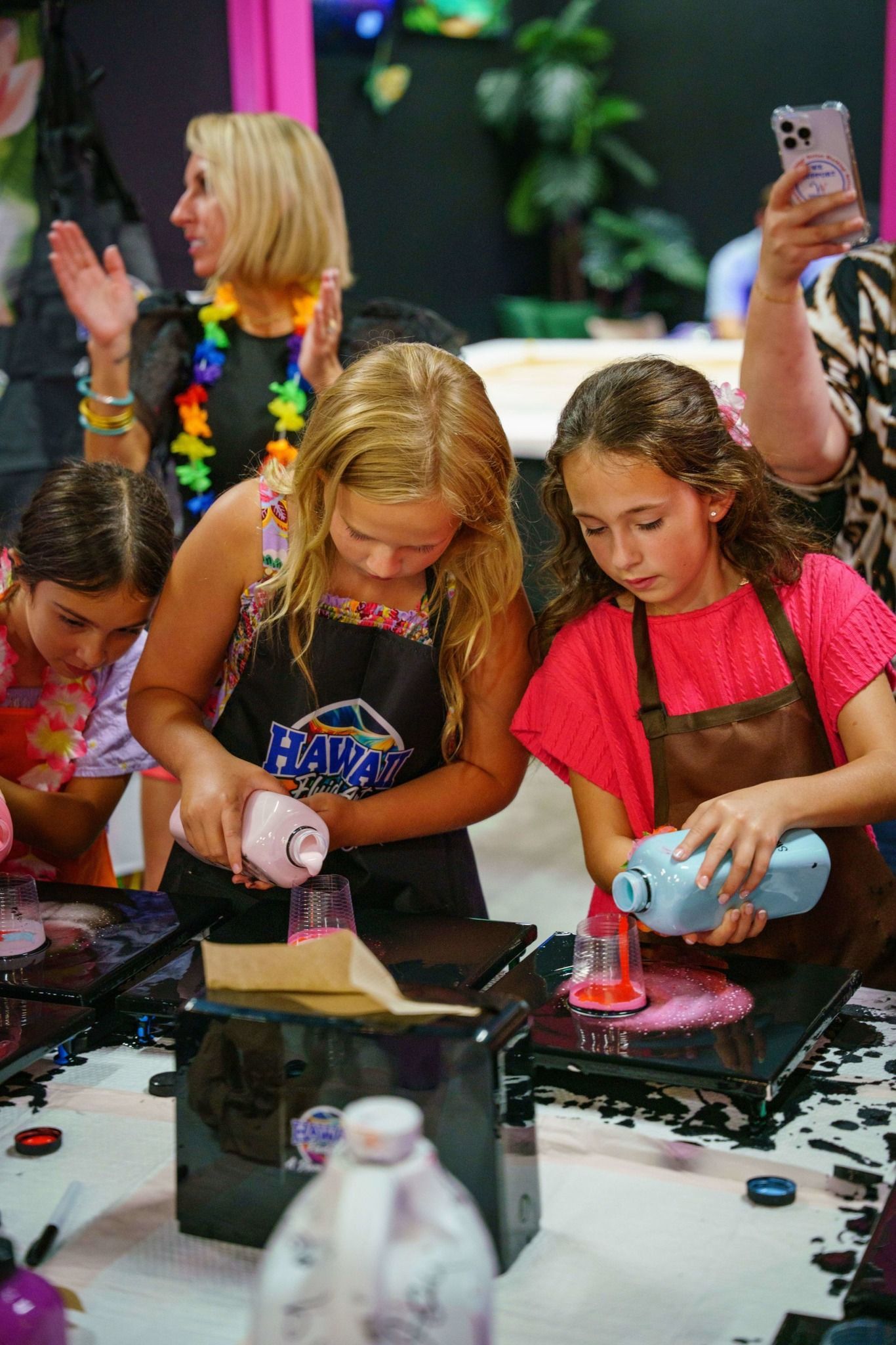 People creating colorful resin art at a table, with a phone recording in the background