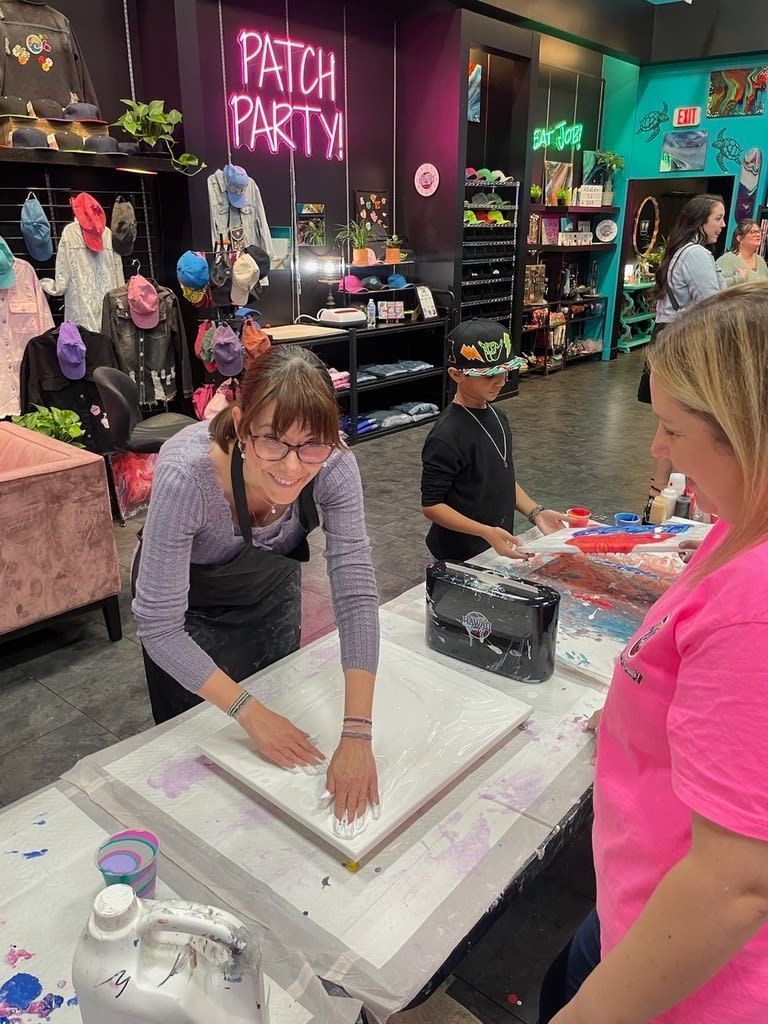 Person in a craft store making slime at a table while another person watches nearby.