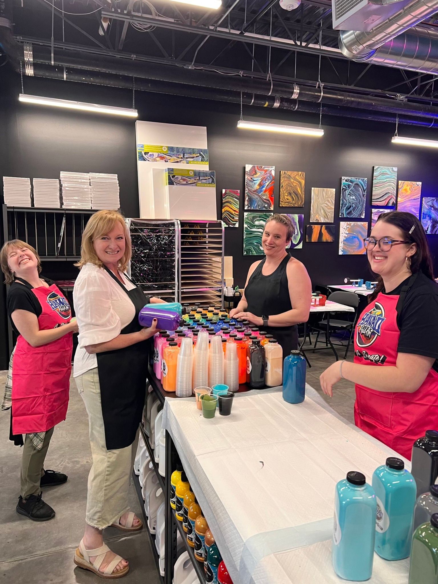 Four women at a table with colorful drink bottles in a bright indoor market booth