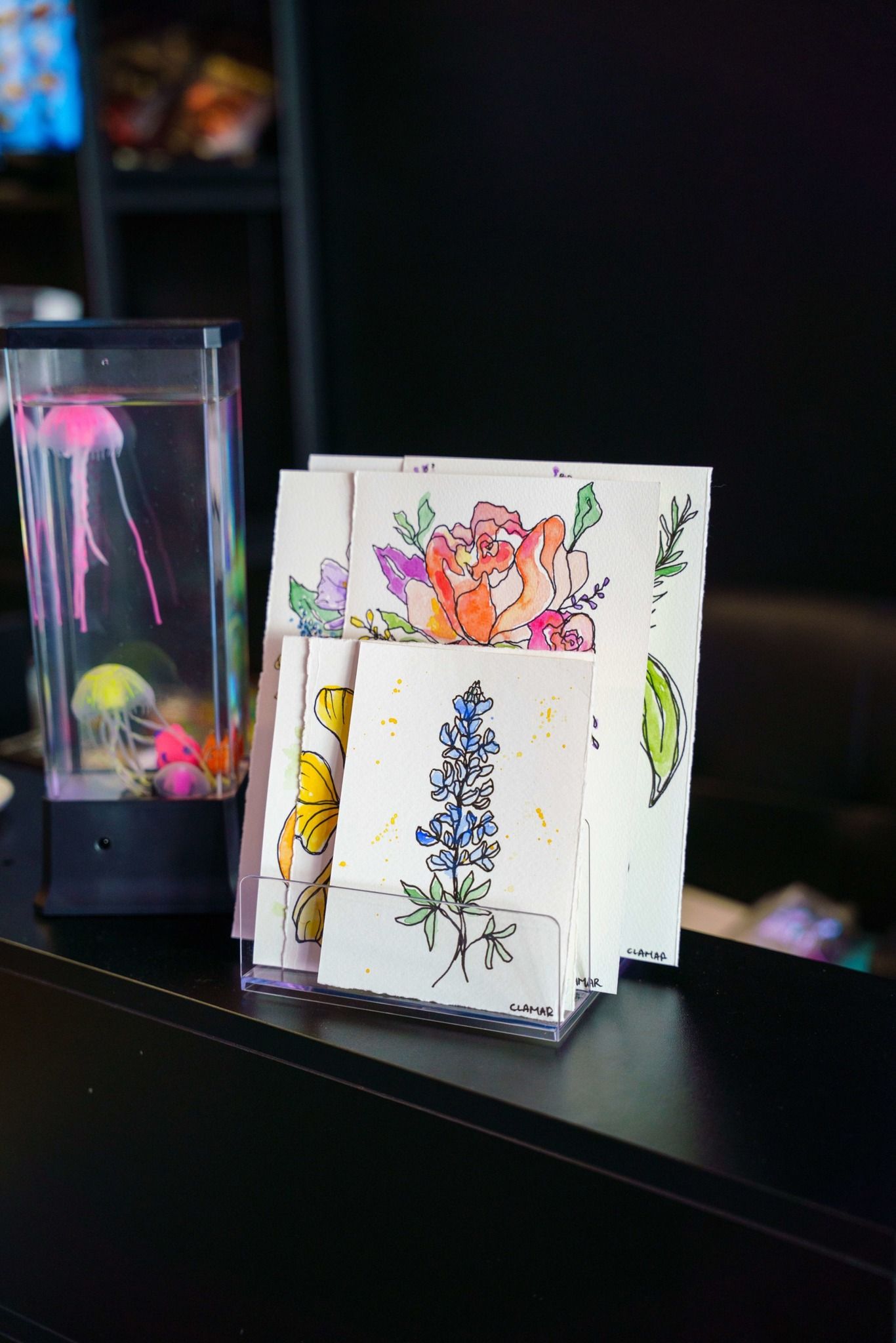 Small folded greeting cards with colorful floral designs displayed on a dark shelf.