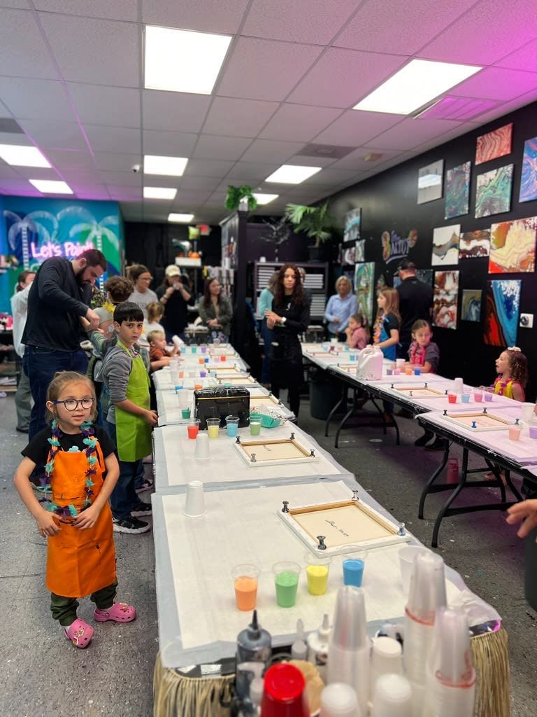 Kids at a birthday party decorating cups and treats at long tables in a colorful indoor space