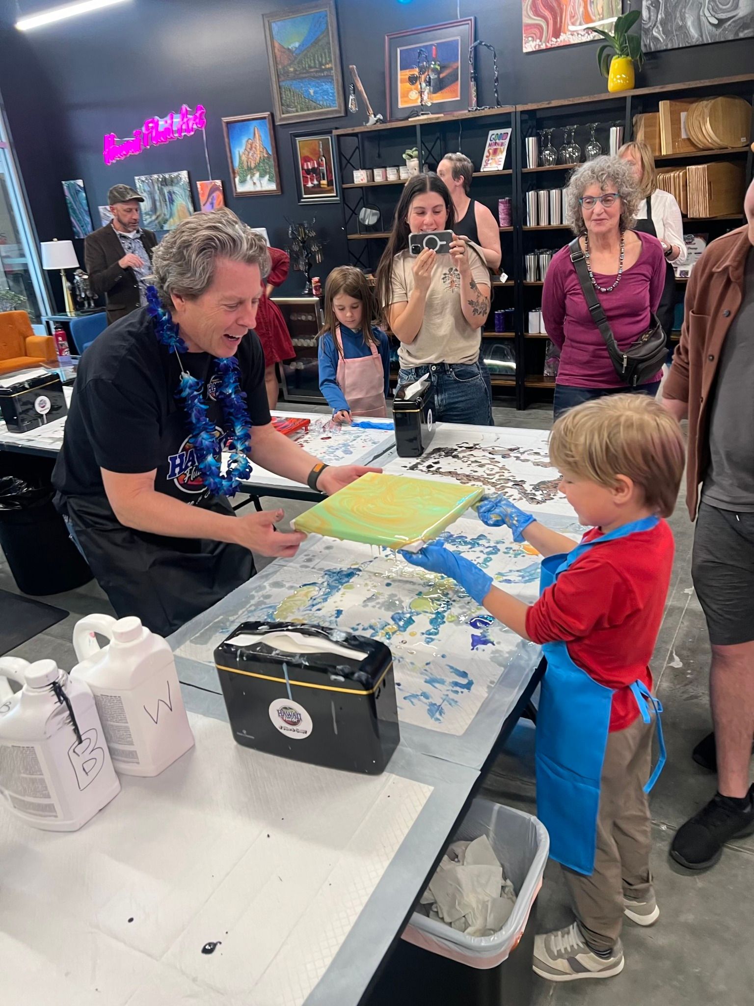 People gathered around a table at a store, with a child and adult exchanging an item during a craft activity.