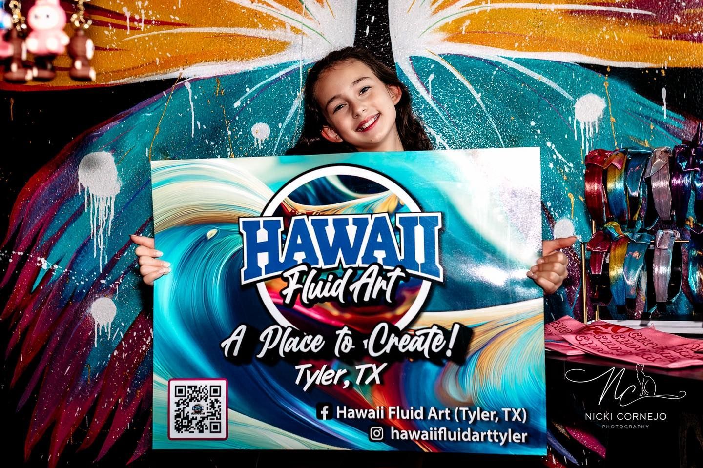 Smiling woman behind a Hawaii Fluid Art sign with bright teal and orange paint splashes
