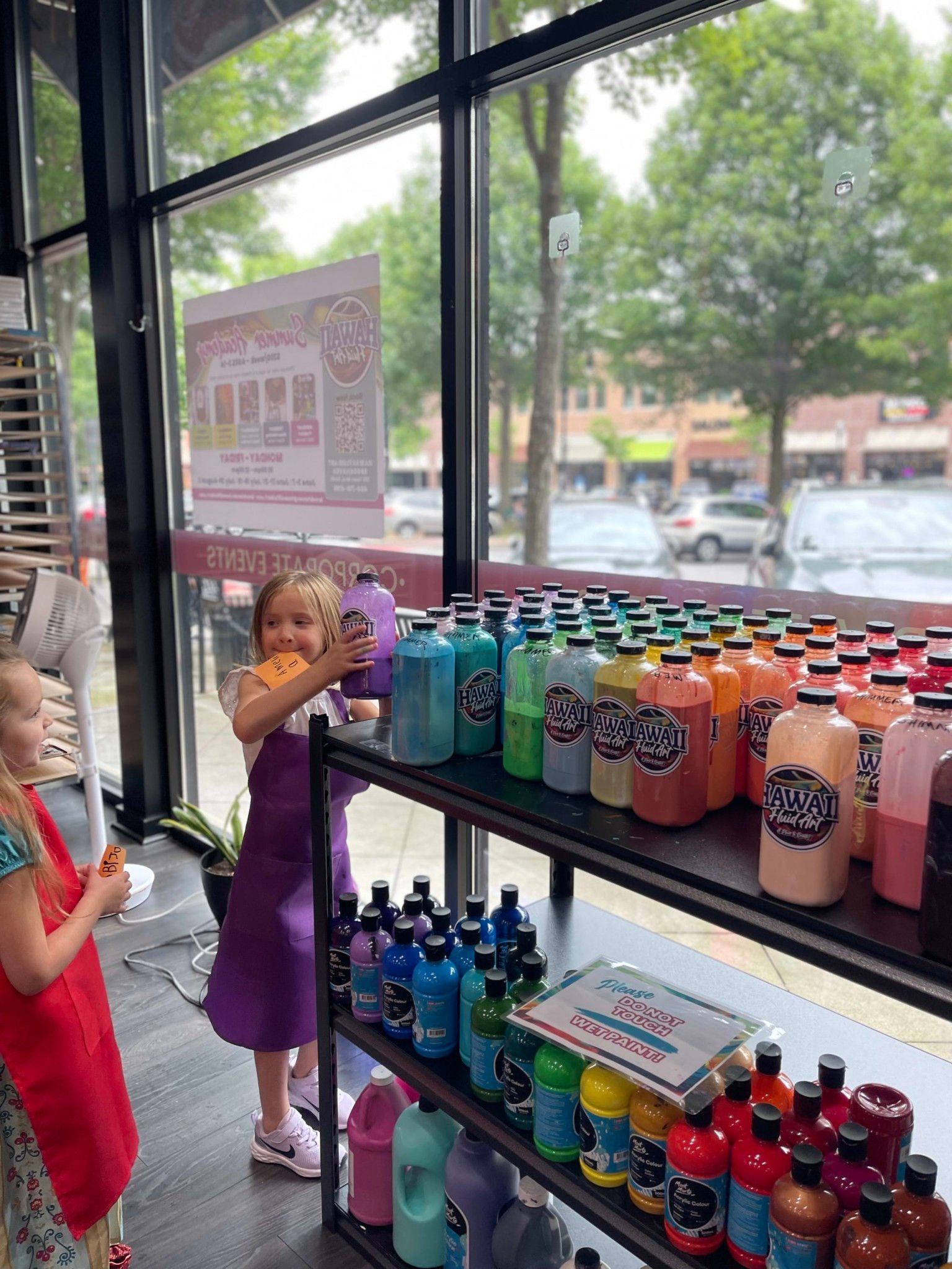 Children browsing colorful drink bottles in a store window display with large street-facing windows.