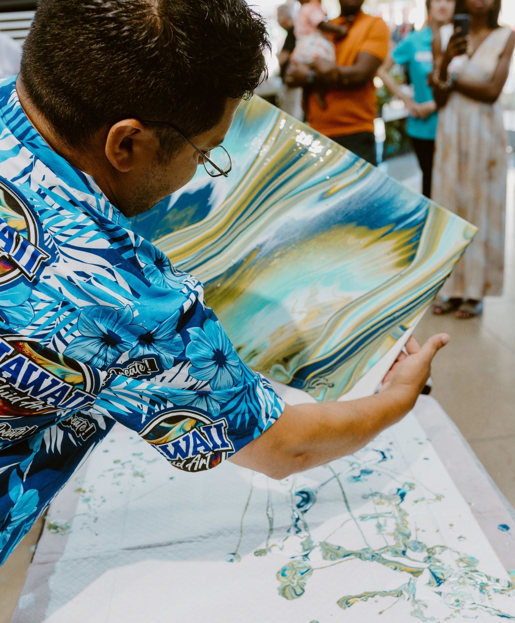 Person in blue patterned shirt unfolding a colorful fabric over a table at a community gathering