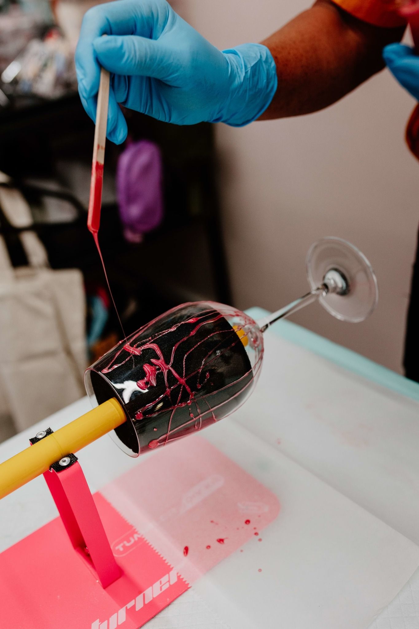 Gloved hands apply red liquid to a glass with a brush on a lab bench