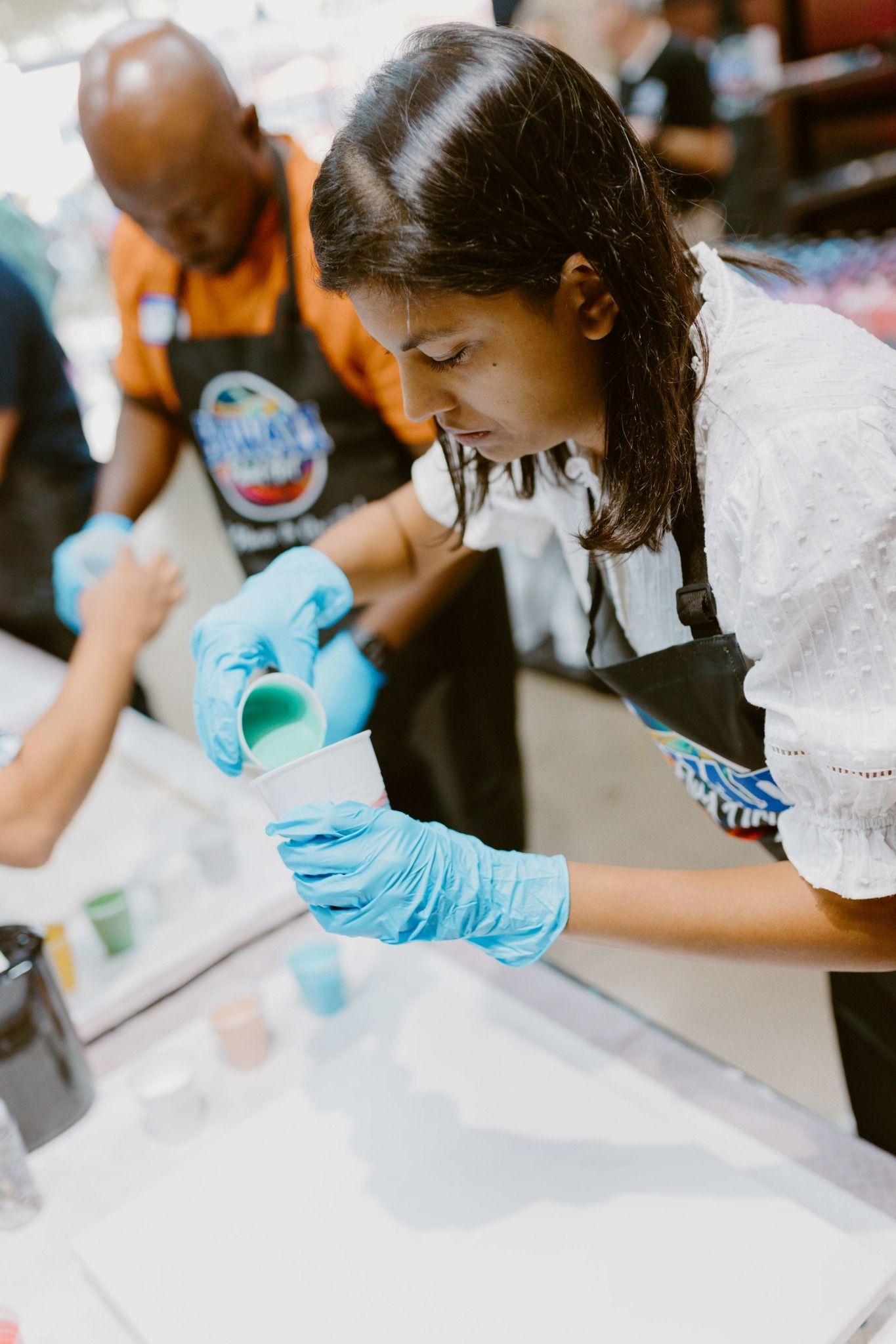 Two people in gloves mixing liquid in a lab container at a table