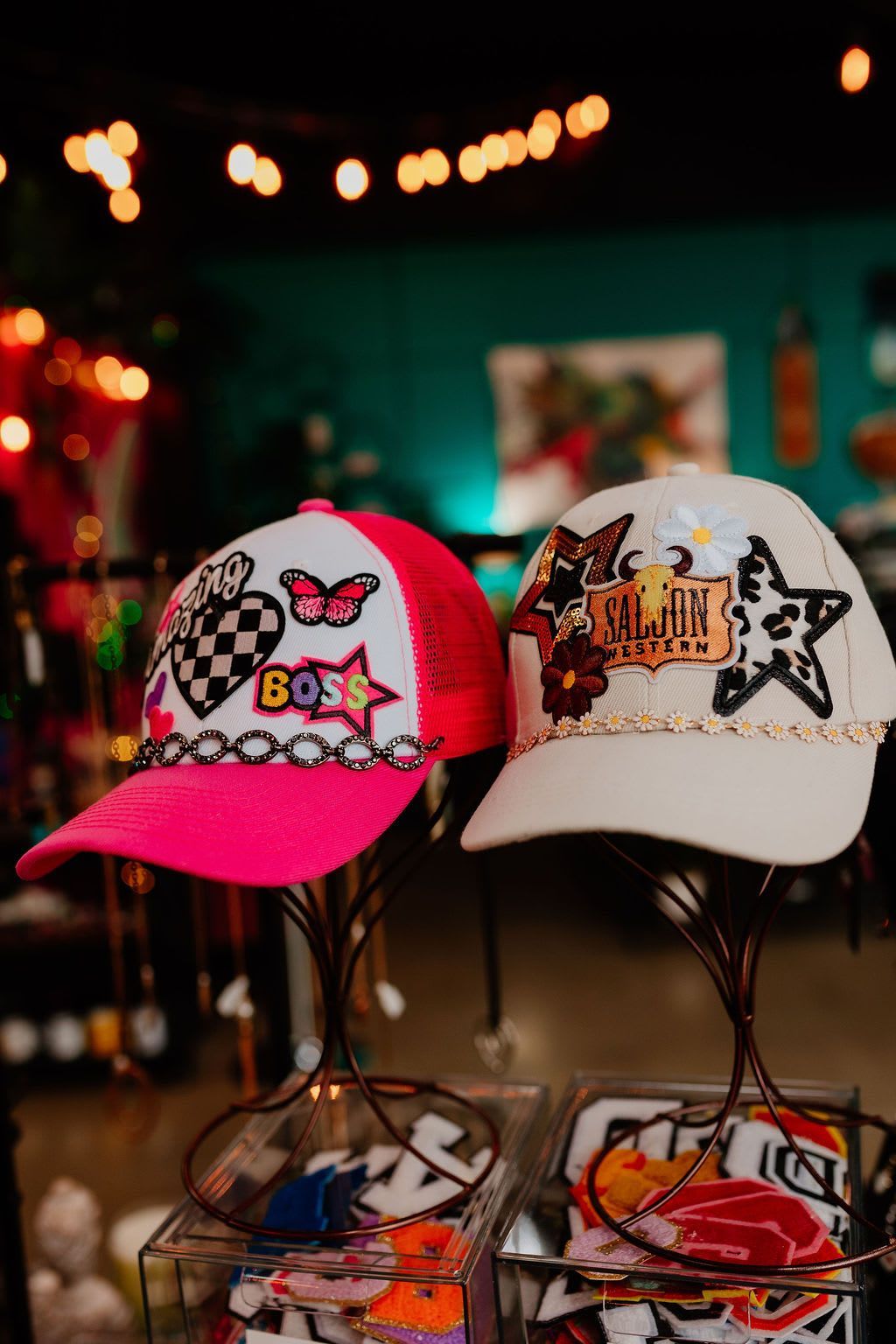 Two colorful embroidered trucker hats on a store display rack, one pink and one white.