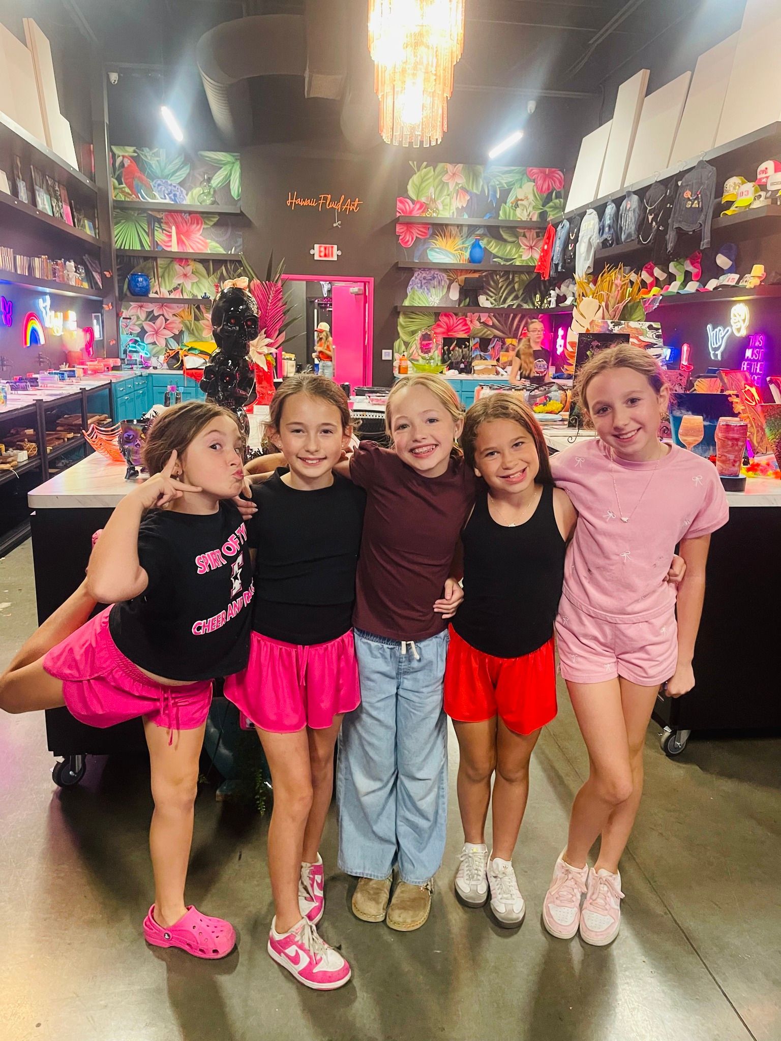 Five children posing arm-in-arm in a colorful store aisle, smiling at the camera.