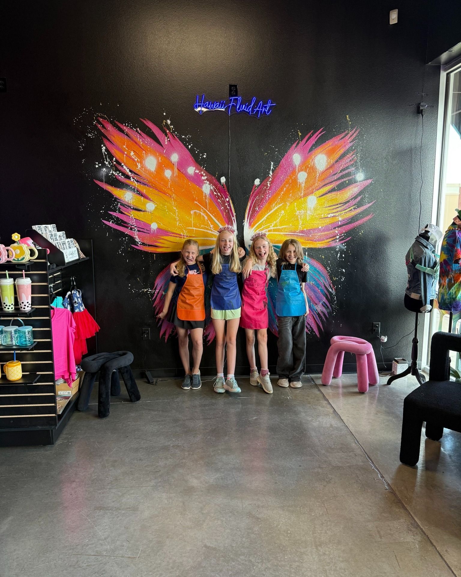 Three people posing in front of colorful butterfly wings mural inside a shop or studio