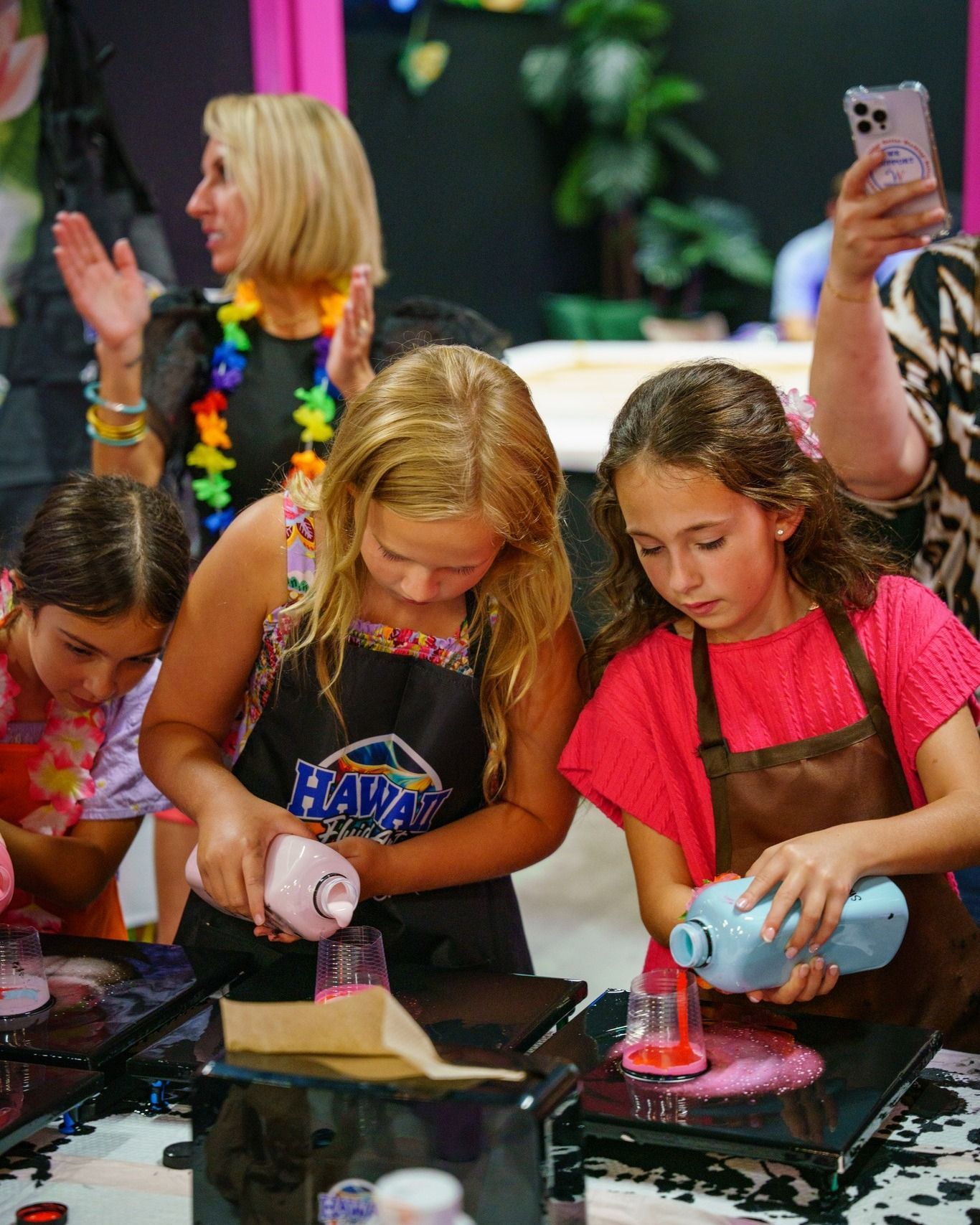 Children pouring colorful liquids into molds at a craft table during a hands-on activity.
