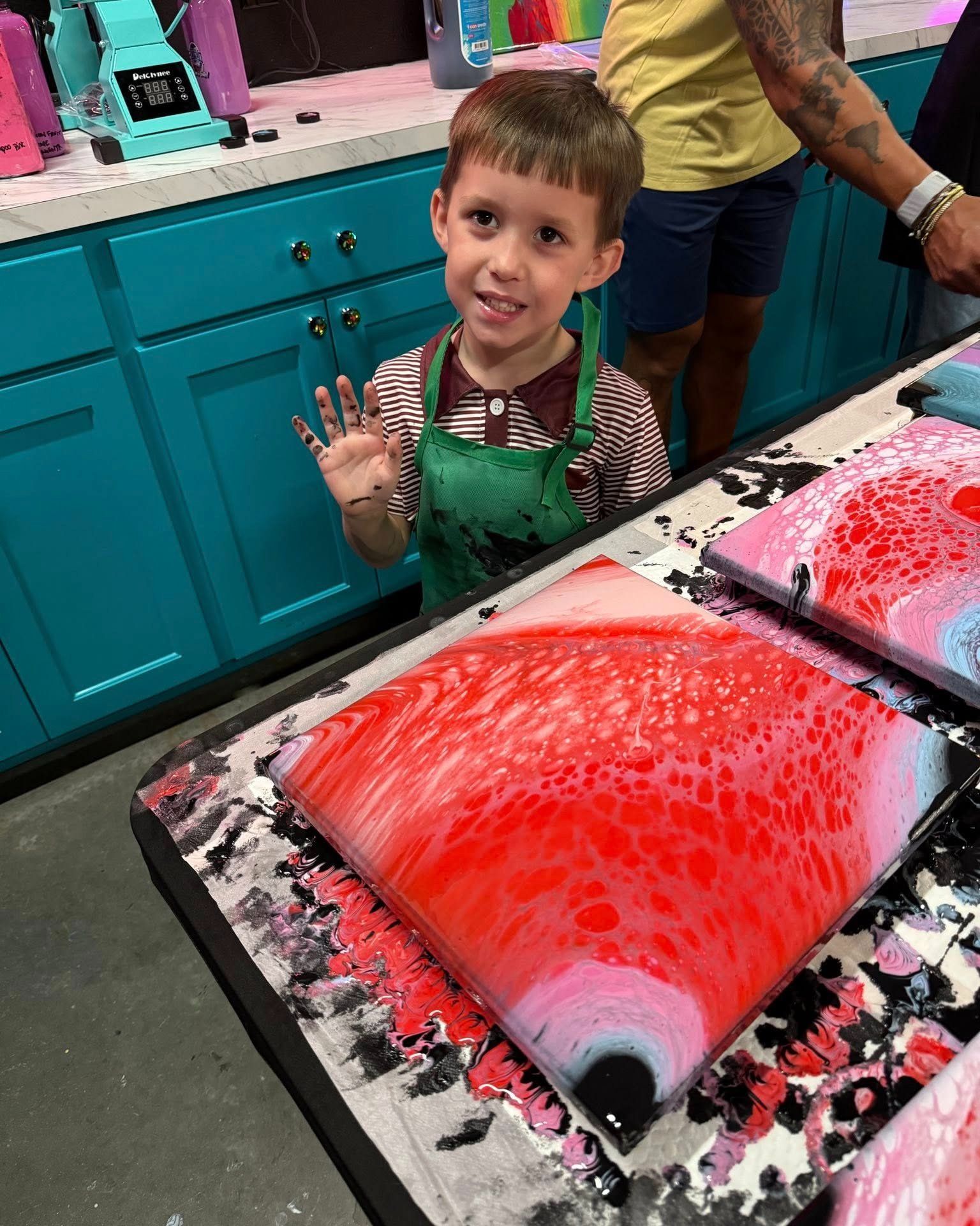 Child in a green apron smiles beside bright red-and-black paint in a colorful craft studio