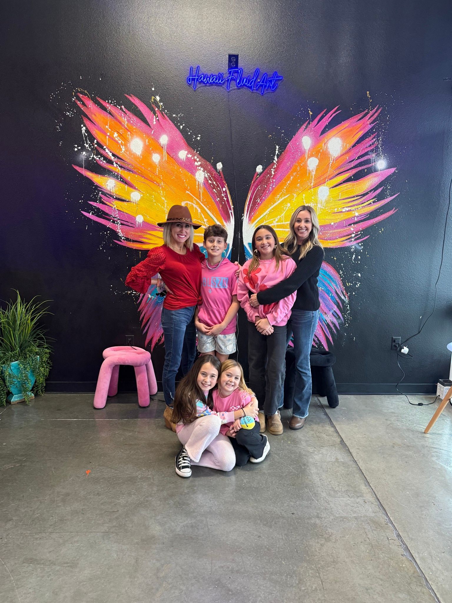 Family posing in front of colorful butterfly wings mural, with two children sitting in front.