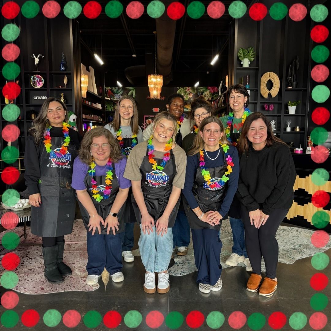 Six people in colorful leis pose together in a decorated shop entrance with red and green garland border.