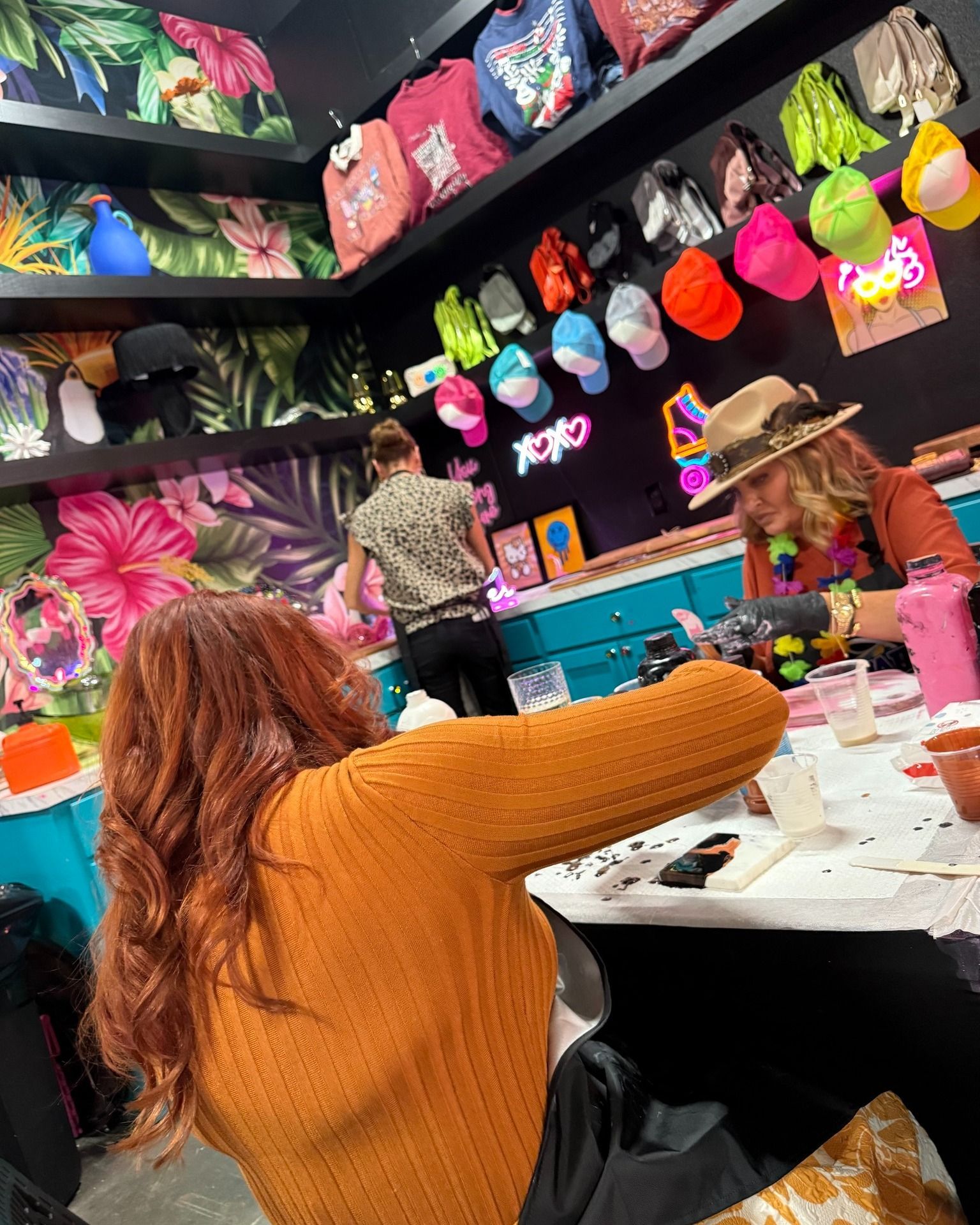 Person painting at a table in a colorful craft shop with bright handbags on the wall