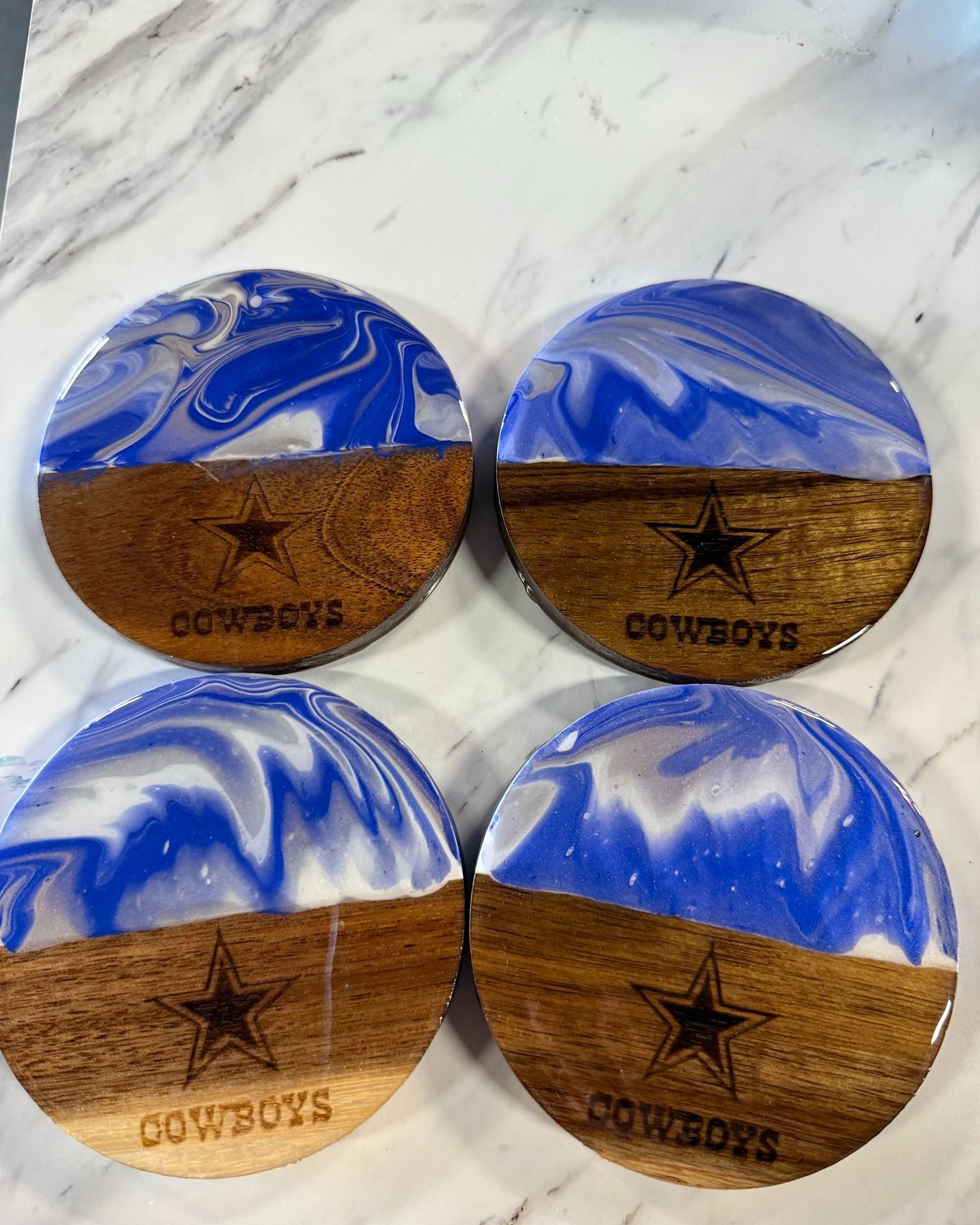 Four round Dallas Cowboys-themed coasters with blue and white marbled tops and cork bottoms on a marble surface