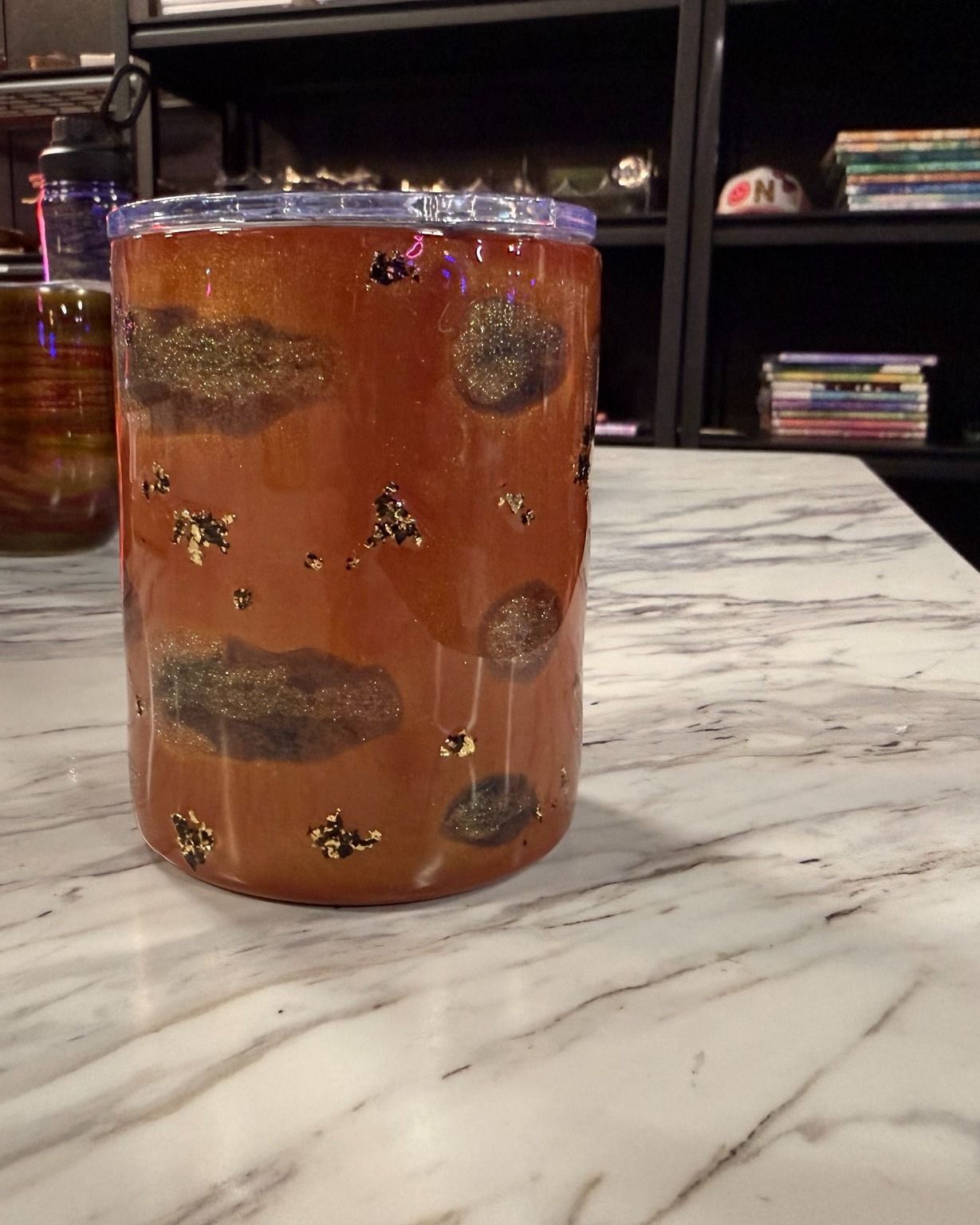 Amber drink in a clear glass on a marble countertop, decorated with flowers and bees.
