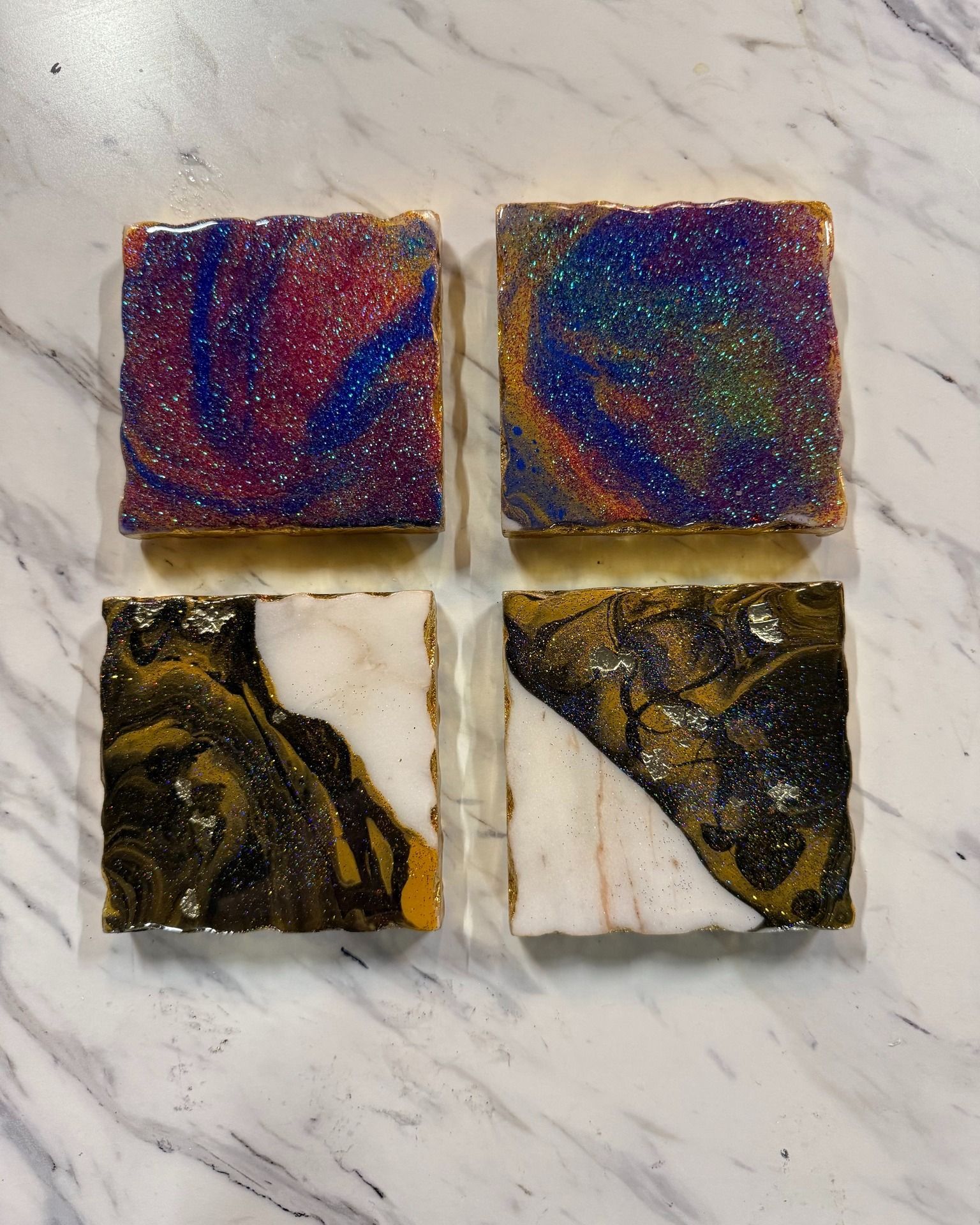 Four glittery square tiles on marble, two red-blue and two black-gold with white centers