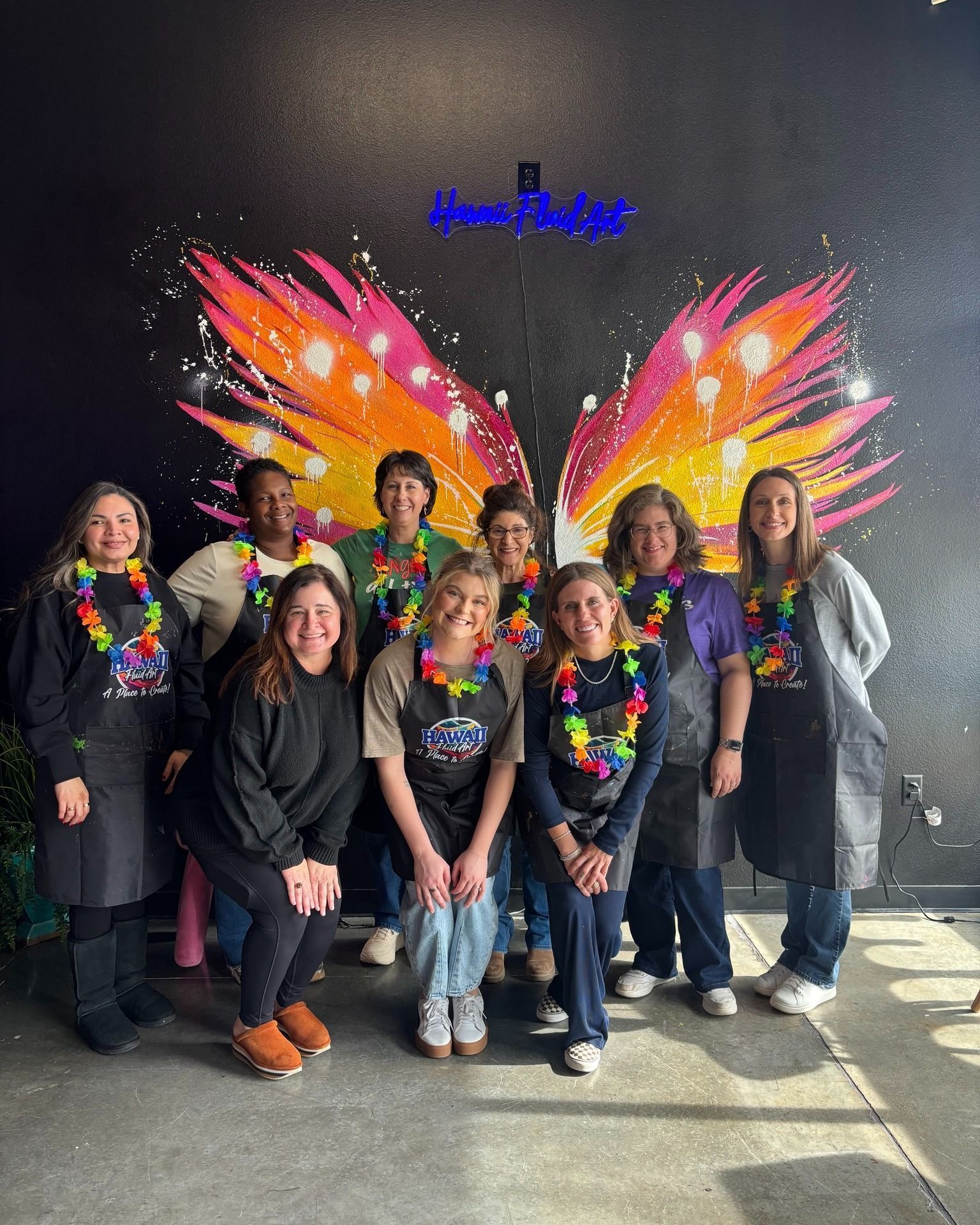 Group of people posing in front of a colorful wing mural, wearing rainbow shirts and smiling.