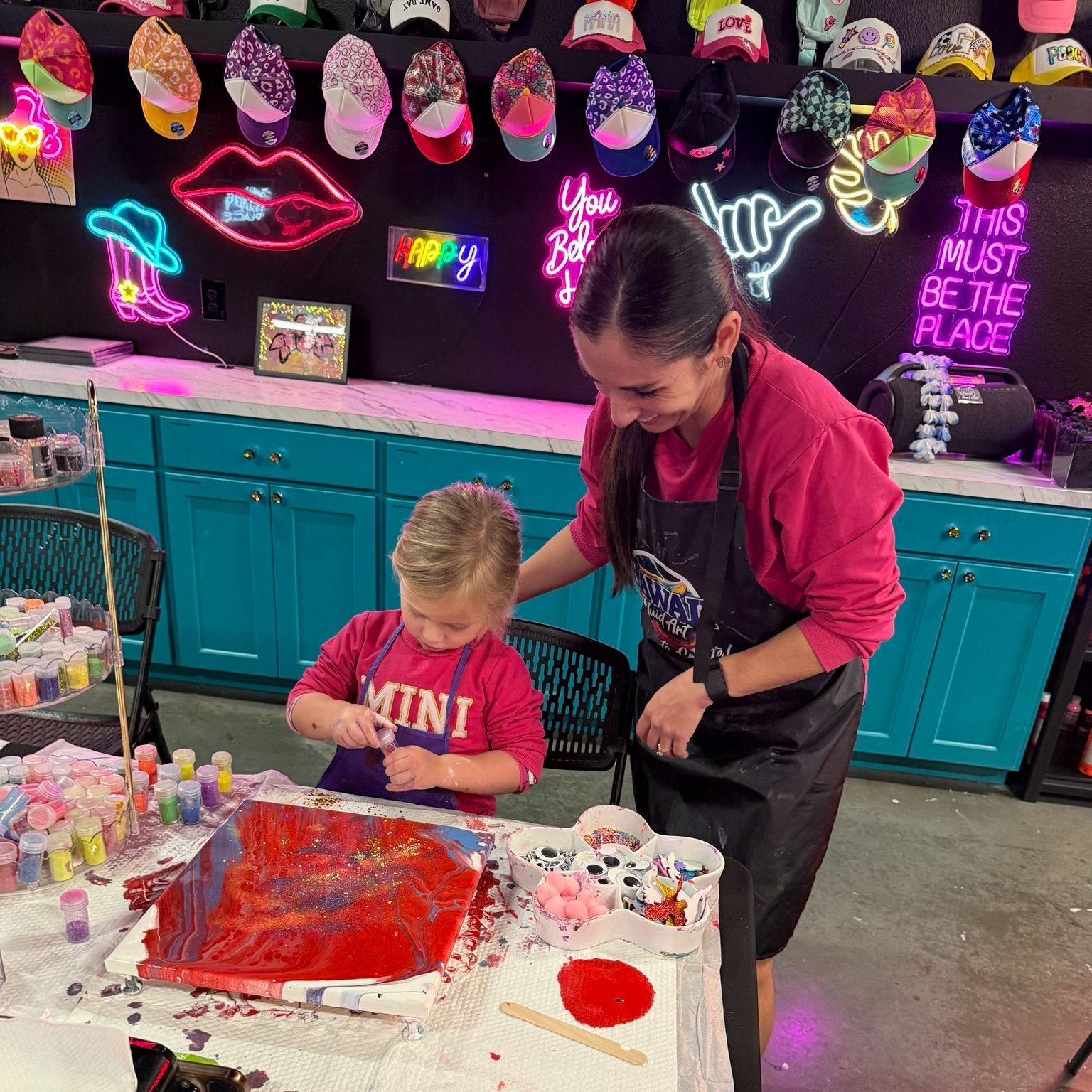 Child and adult decorating a red art project at a craft table with neon decorations in the background