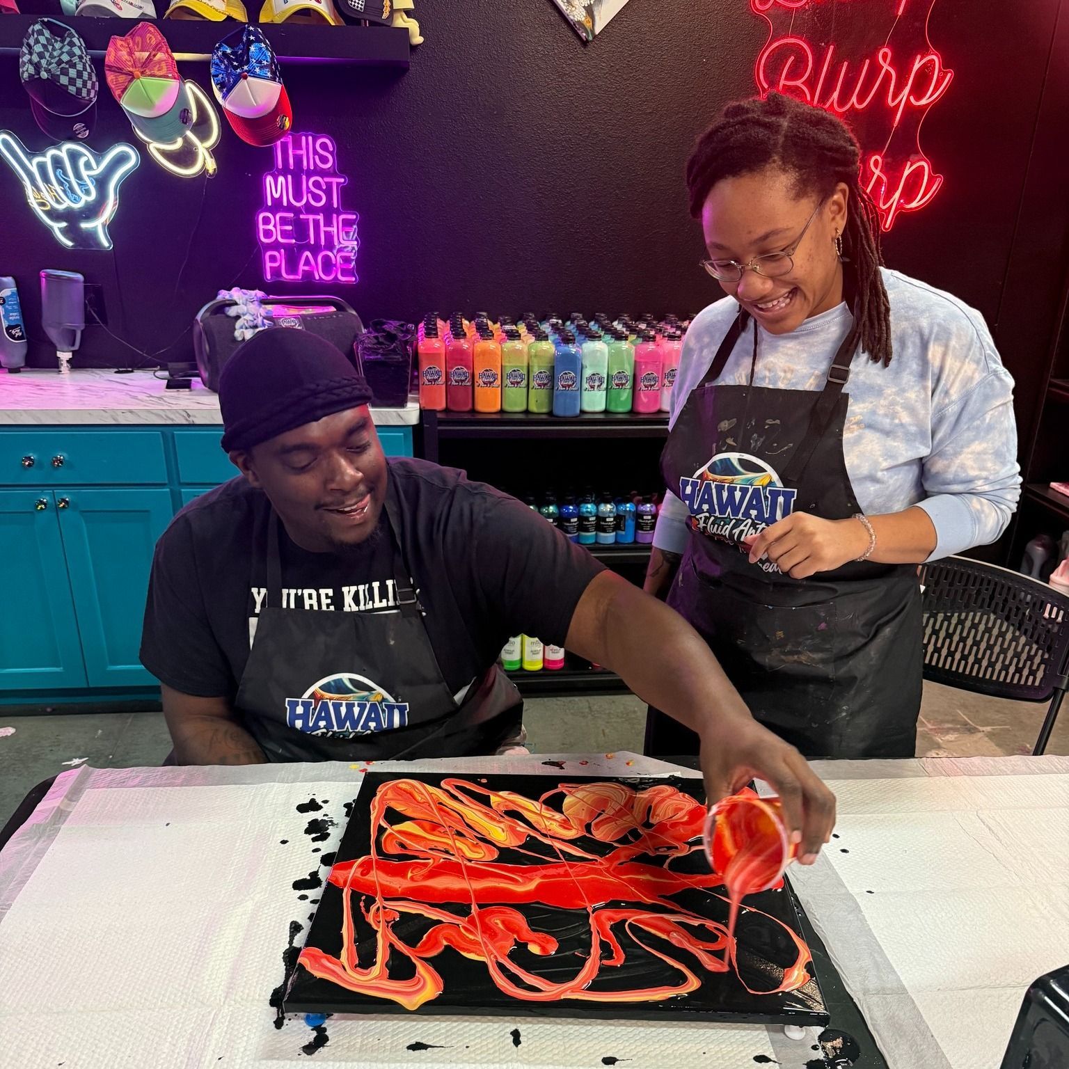 Two people decorating a cake with red icing in a colorful bakery kitchen