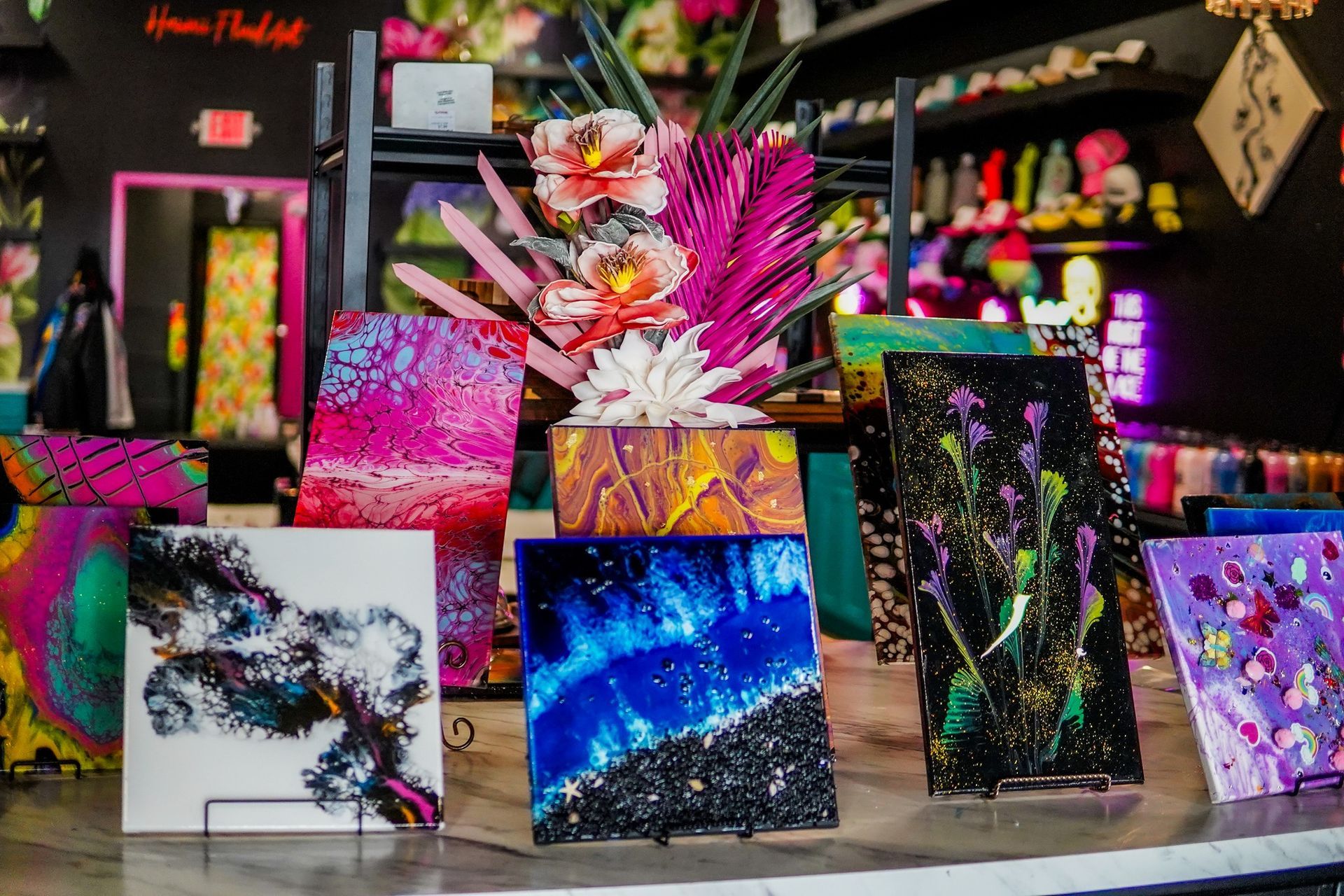 Colorful abstract paintings displayed on a table in an art studio, with a floral centerpiece behind them