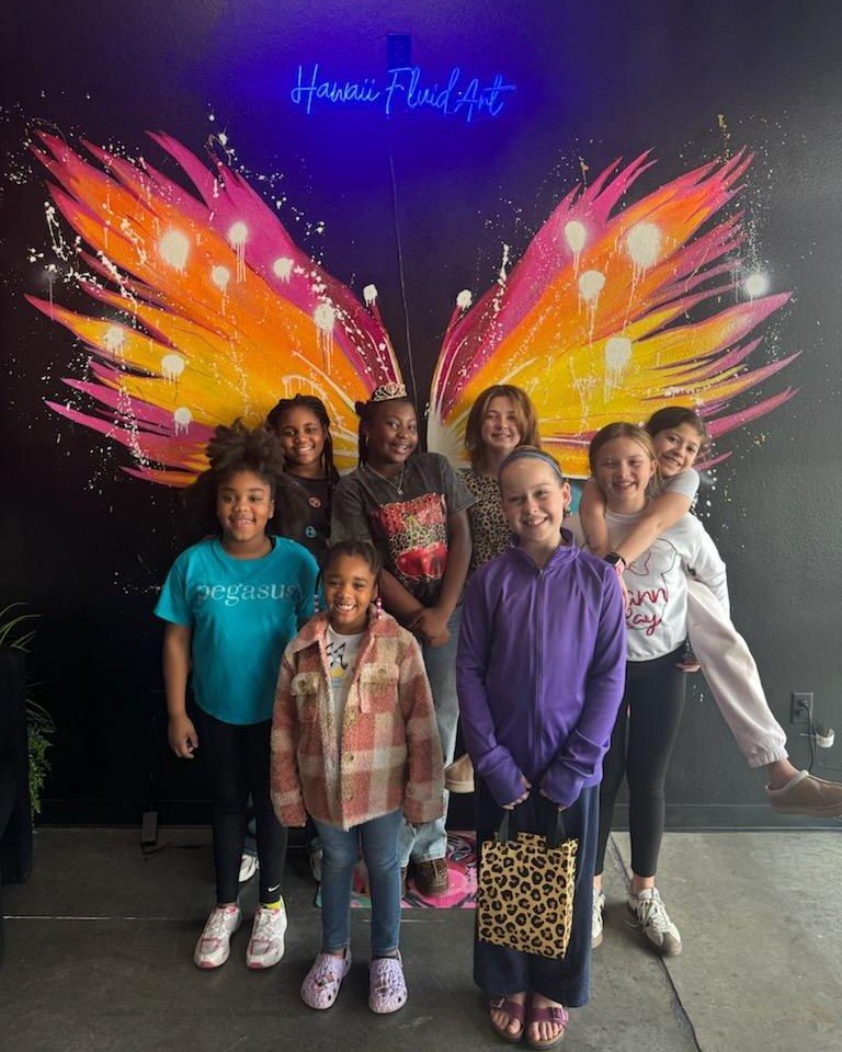 Group of children posing in front of bright pink and orange butterfly wings mural