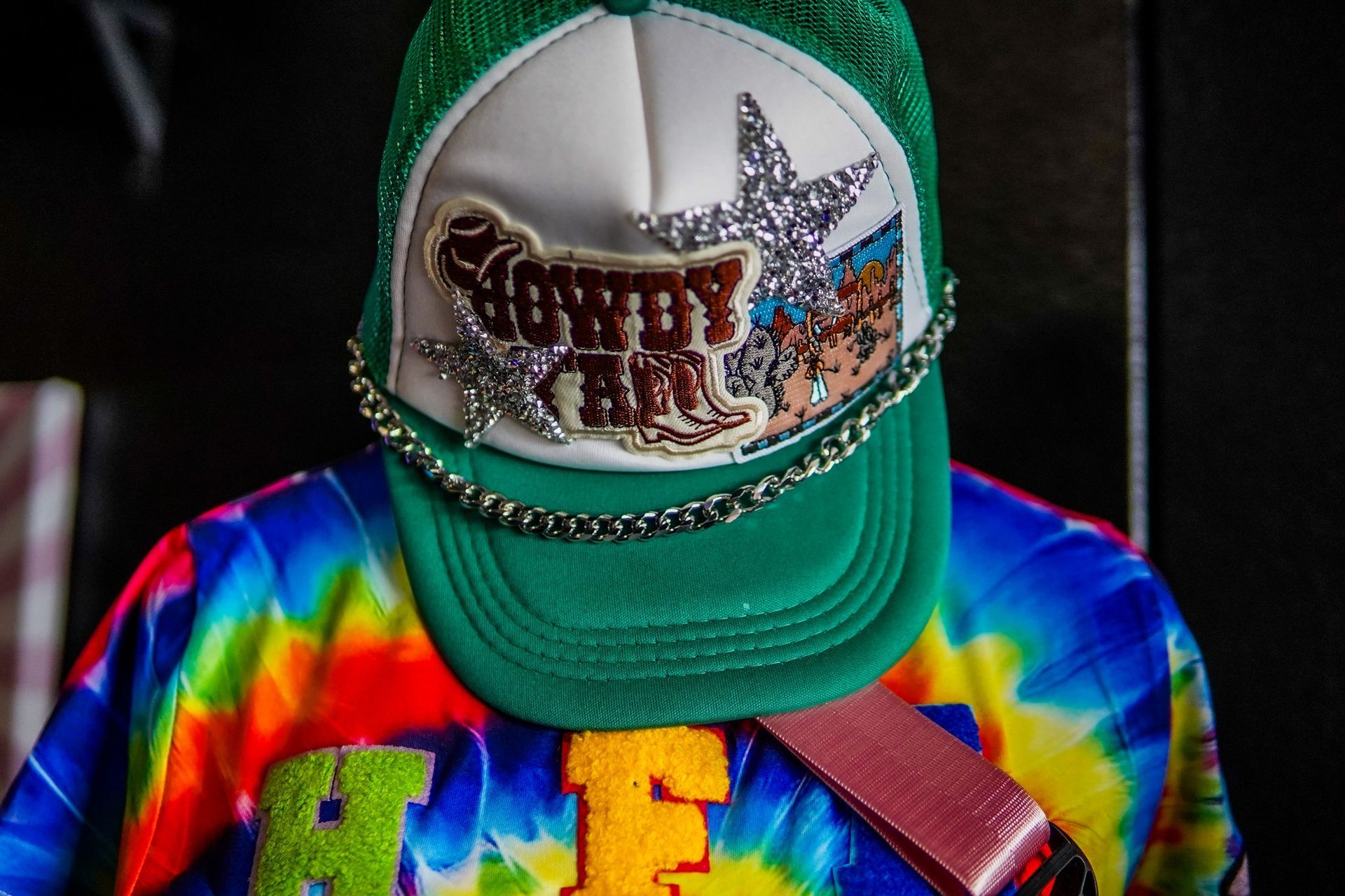 Person in a green cap and rainbow shirt looking down, with a star design on the cap.