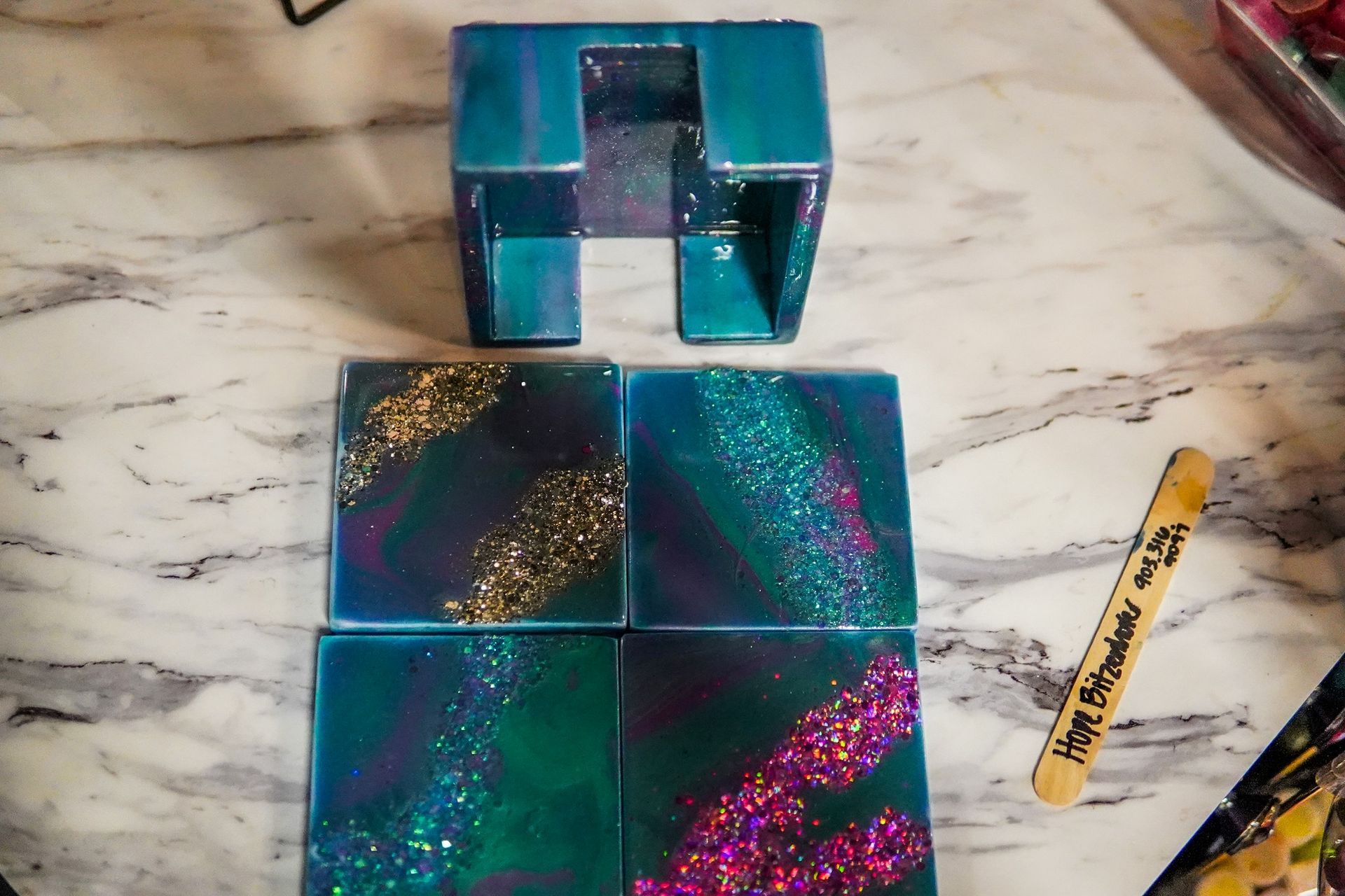 Two iridescent blue-green gift boxes with glittery pink and gold accents on a marble surface