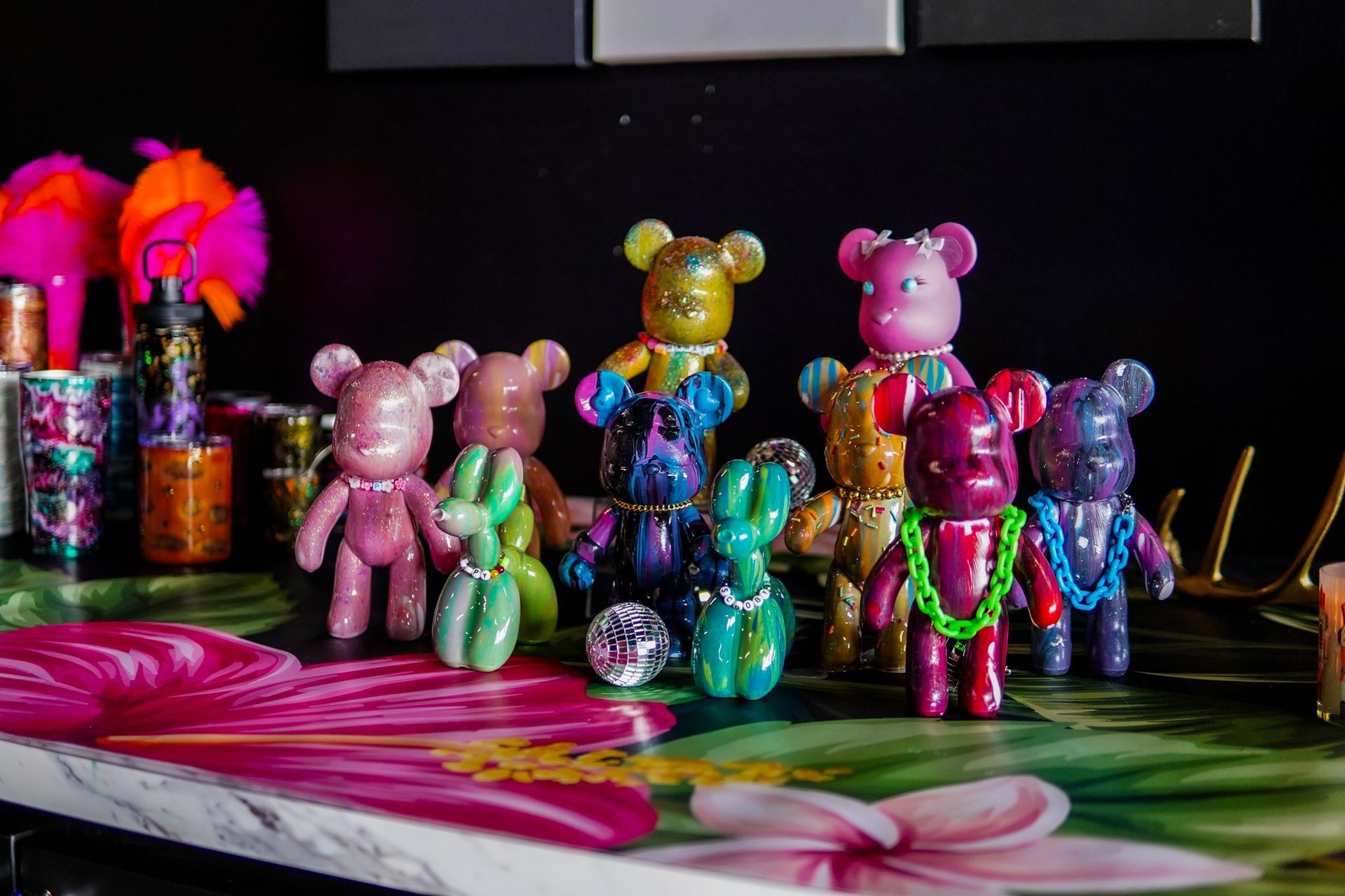 Colorful bear figurines arranged on a reflective surface with a pink floral design, against a dark background