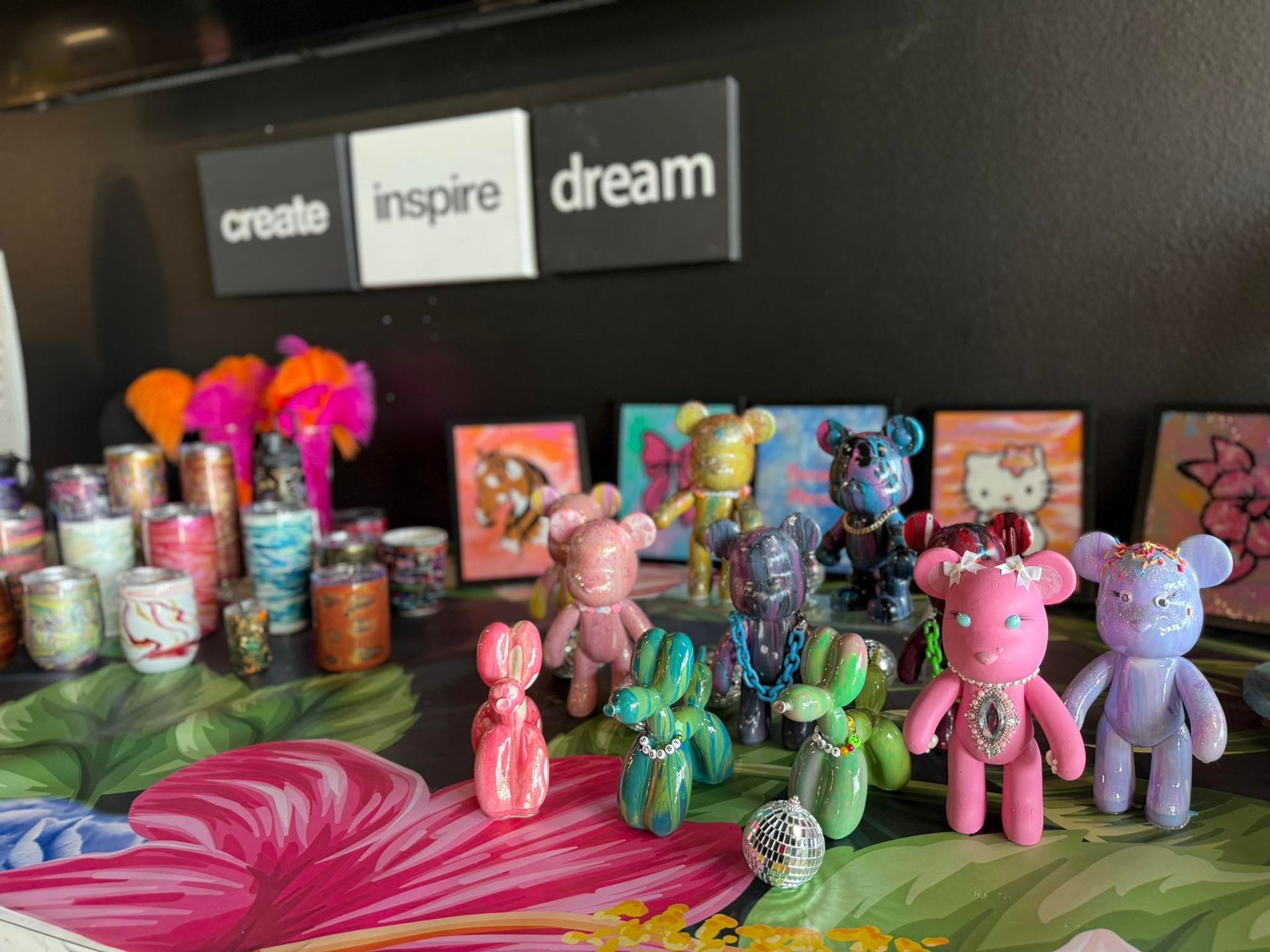 Colorful handmade figurines and tins on a table beneath “create inspire dream” wall signs