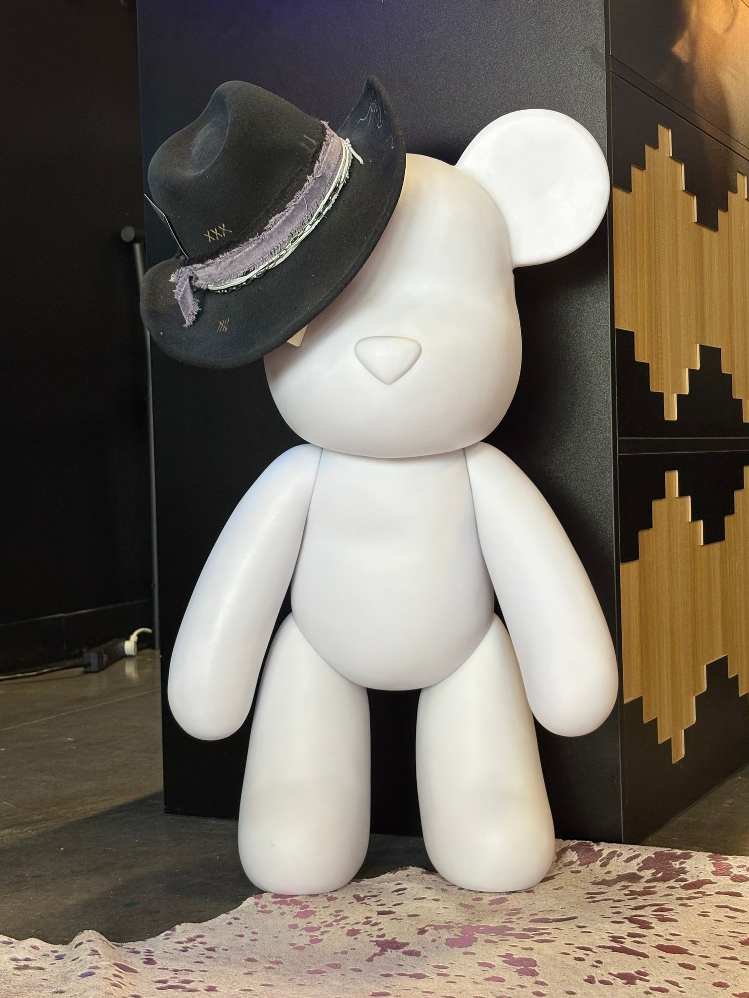 White bear sculpture wearing a black hat, standing indoors beside a patterned wall.