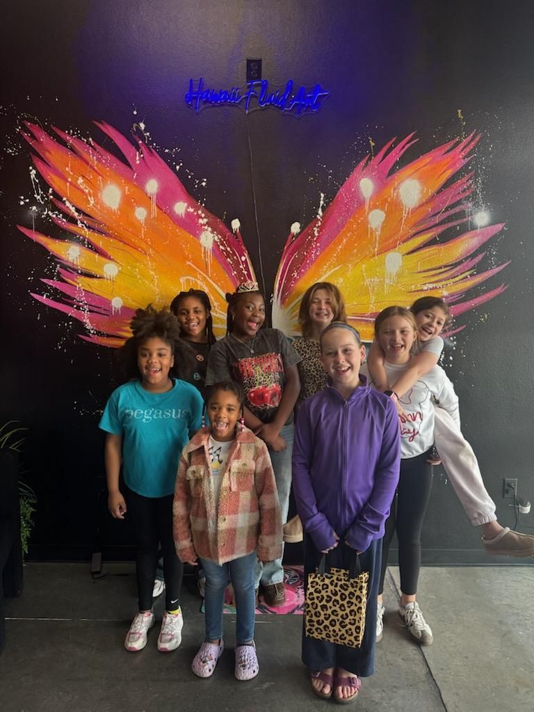 Children posing in front of colorful butterfly wings mural on a dark wall