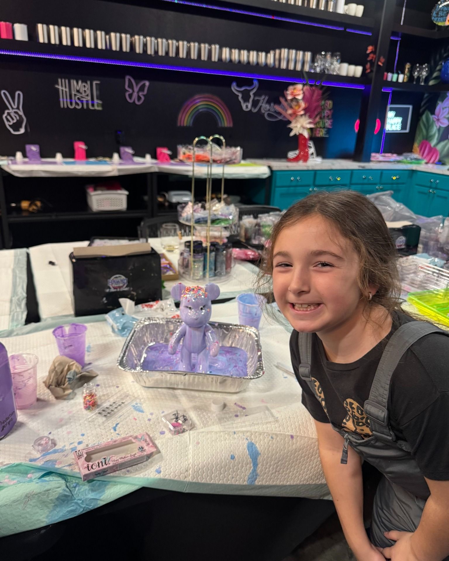 Girl smiling beside purple unicorn crafts at a decorated party table.