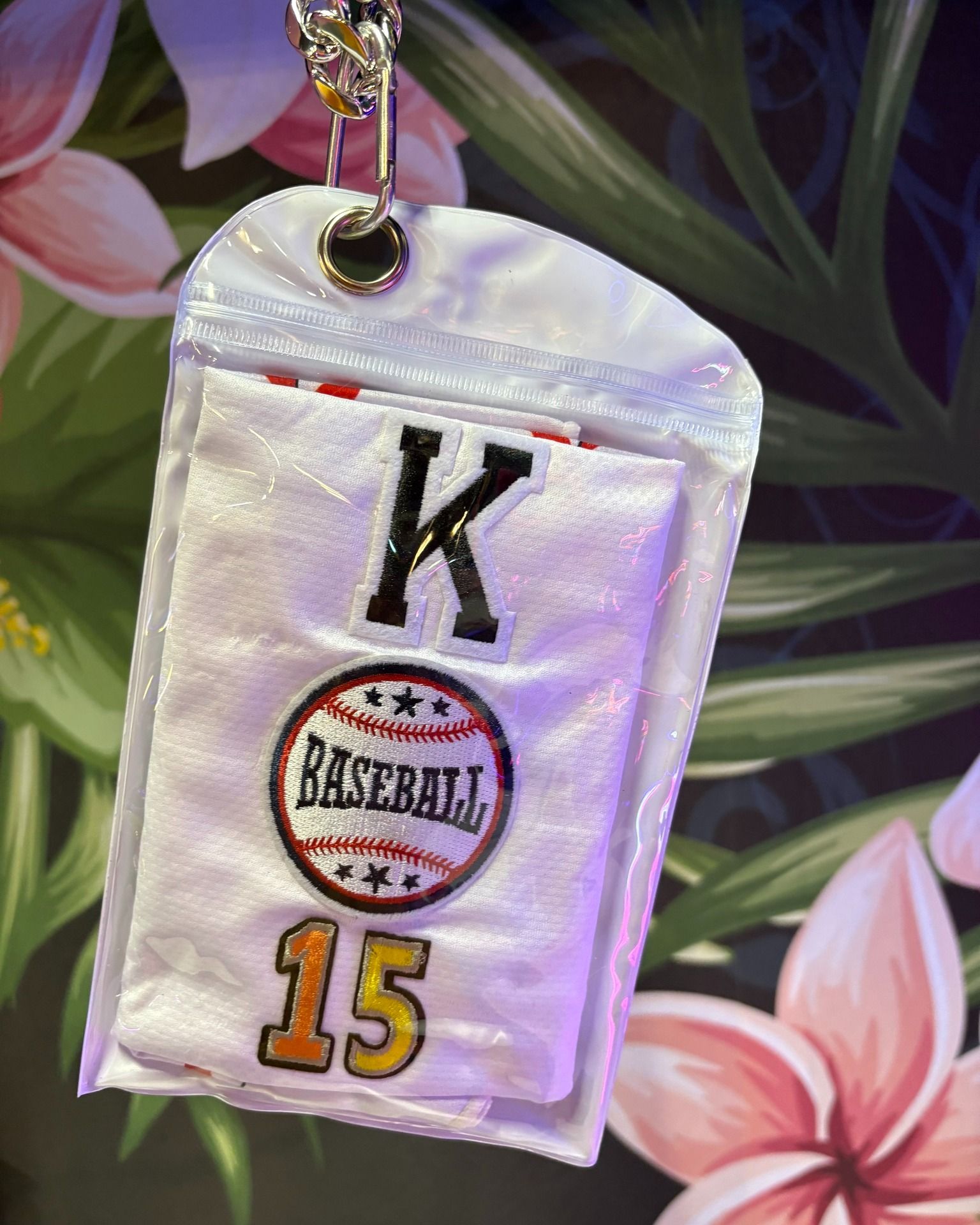 White personalized pendant with a black K, circular logo, and gold 15 on a floral background
